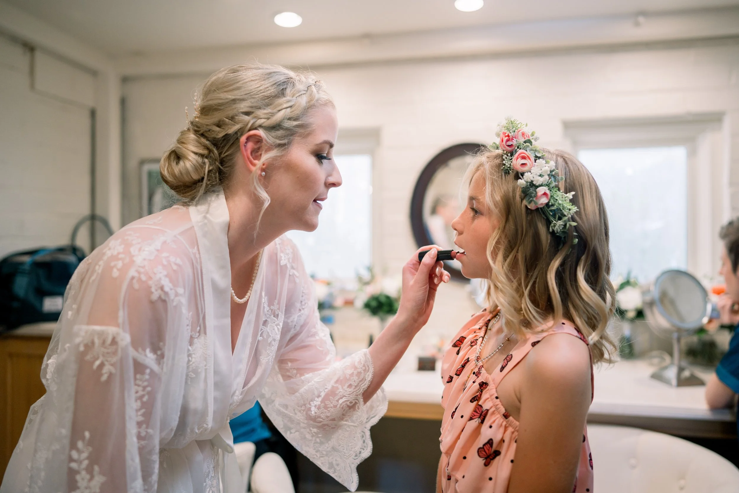 Bride helping a flower girl apply lipstick during a sweet getting-ready moment before the wedding