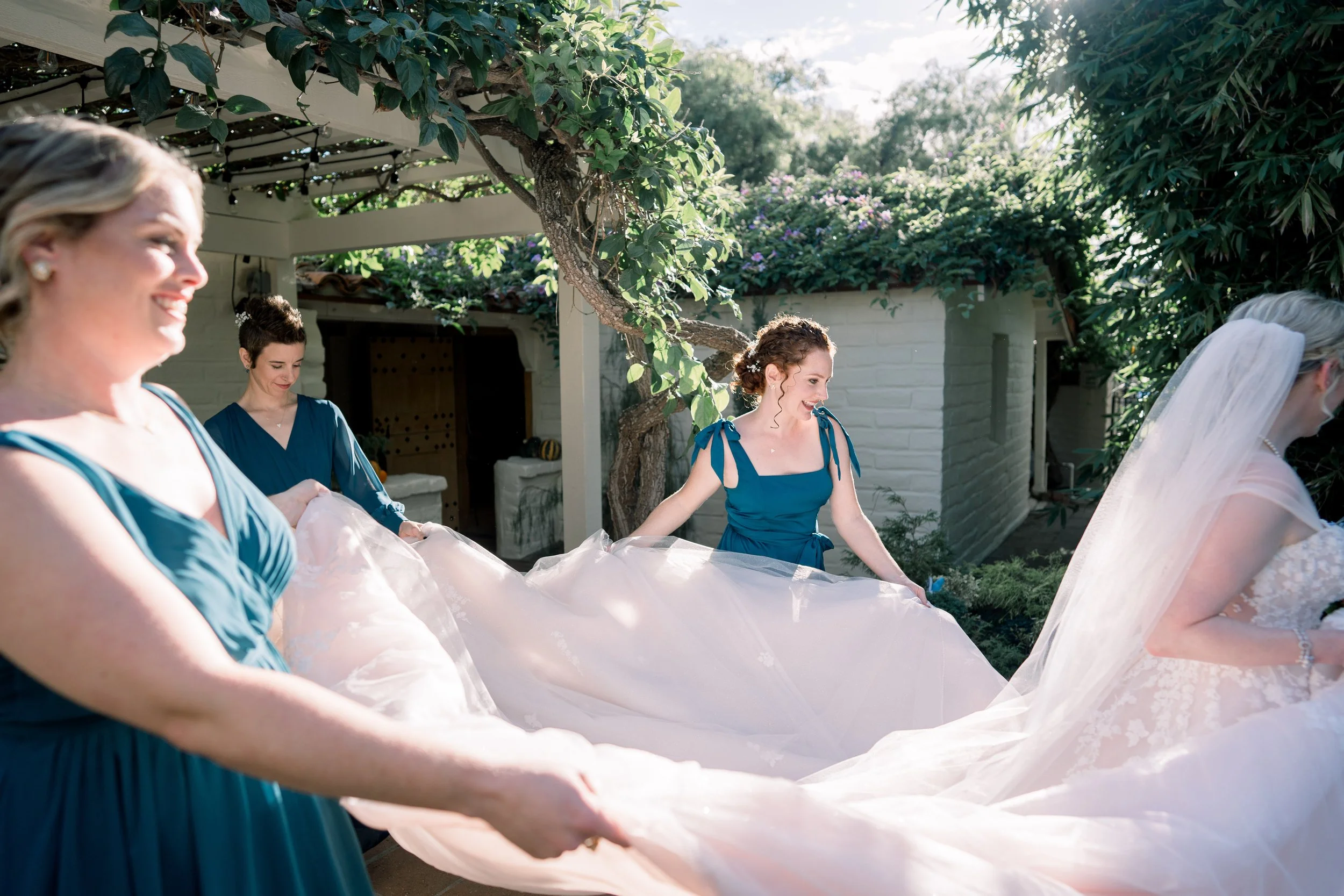 Bridesmaids adjusting and fluffing the bride’s wedding dress and veil before portraits