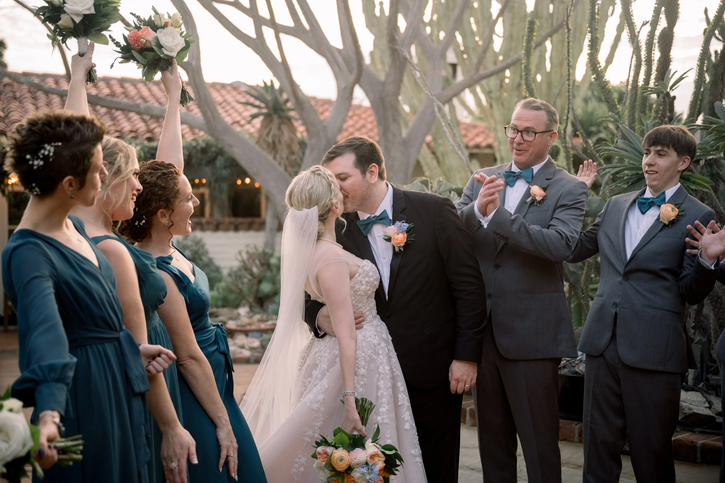 Bride and groom sharing their first kiss while the wedding party cheers and celebrates around them