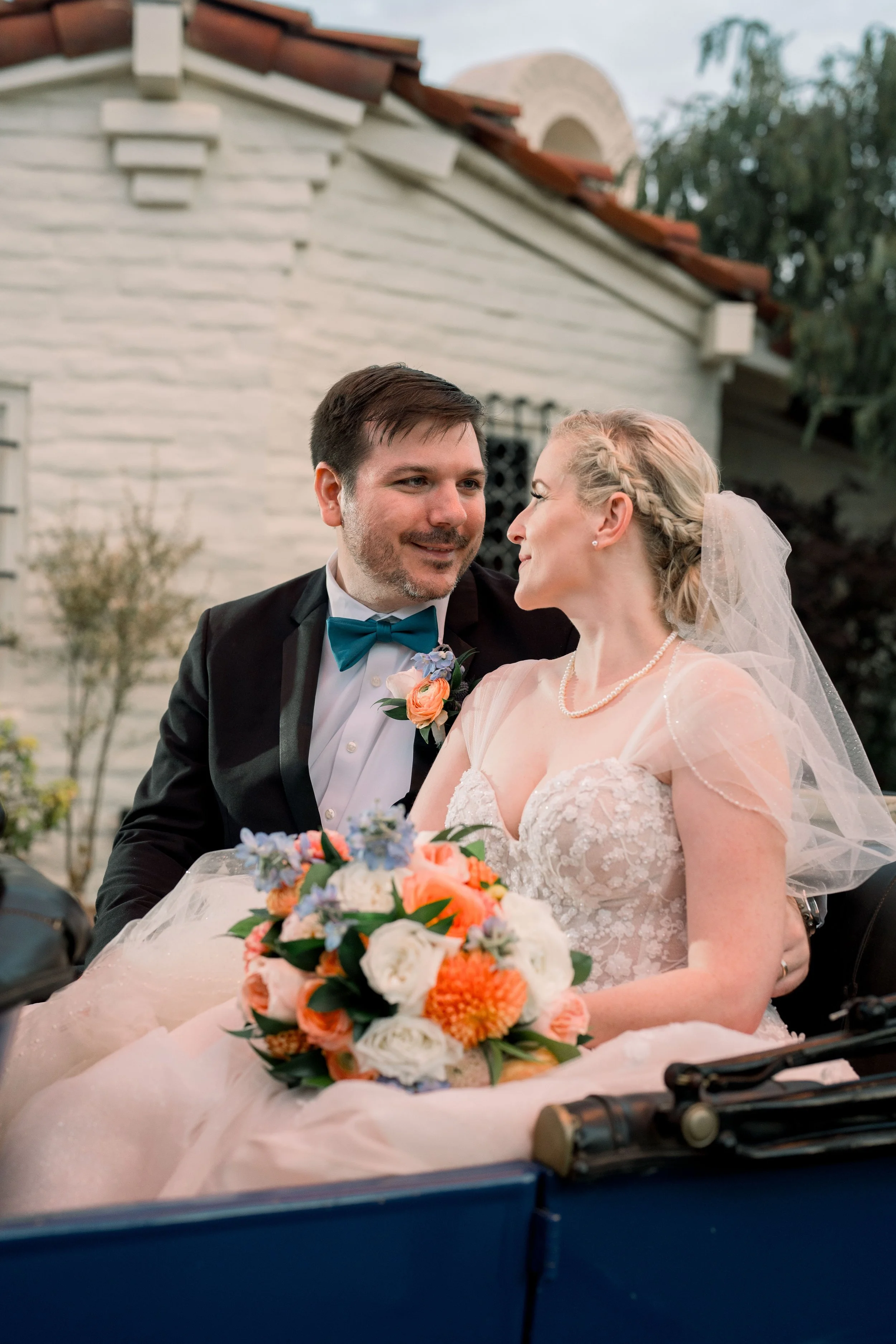 Newlywed couple sitting together in a vintage convertible holding a colorful wedding bouquet