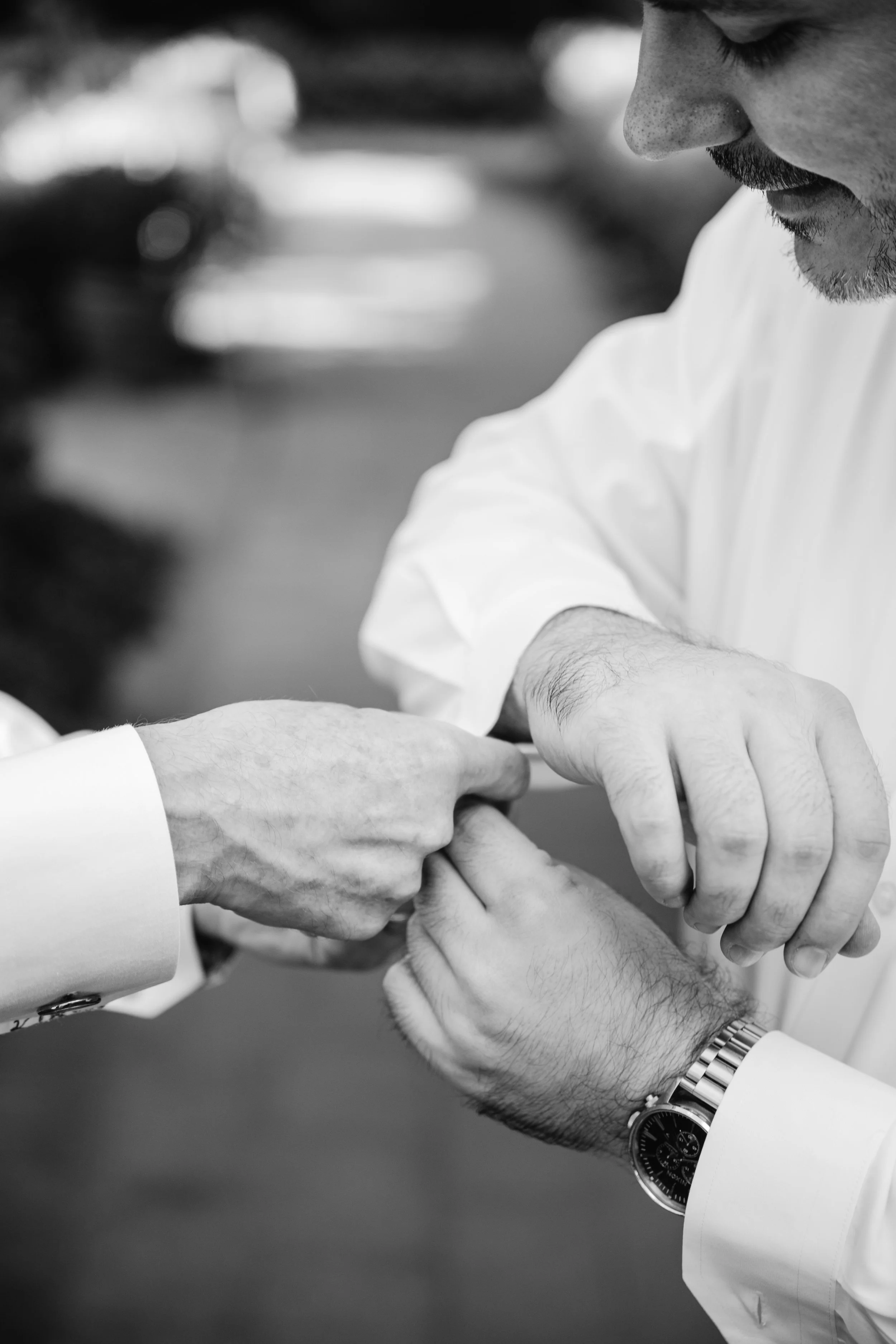 Black-and-white close-up of the groom adjusting cufflinks while getting ready before the ceremony