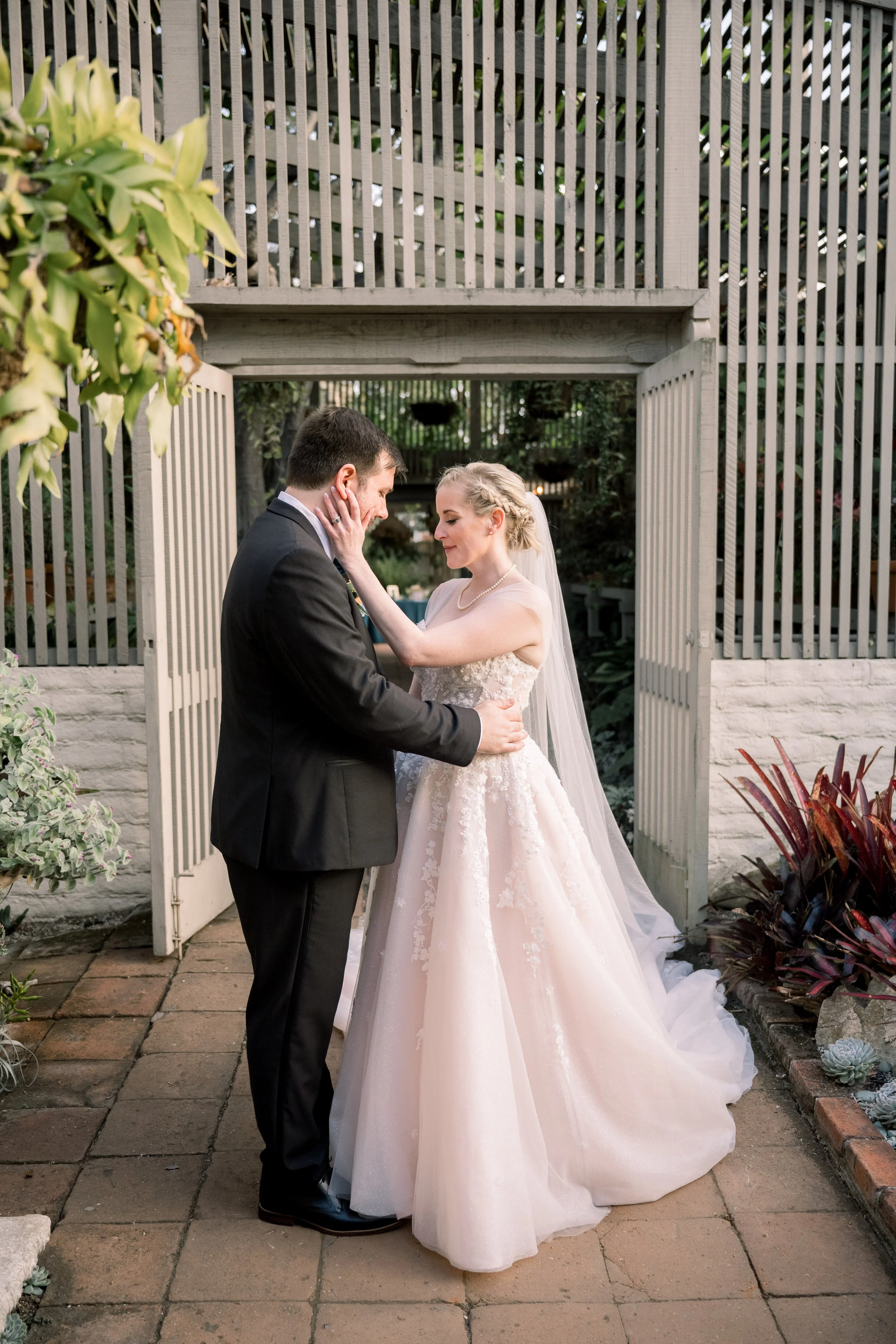 Bride and groom embracing for a romantic wedding portrait in front of an open garden gate