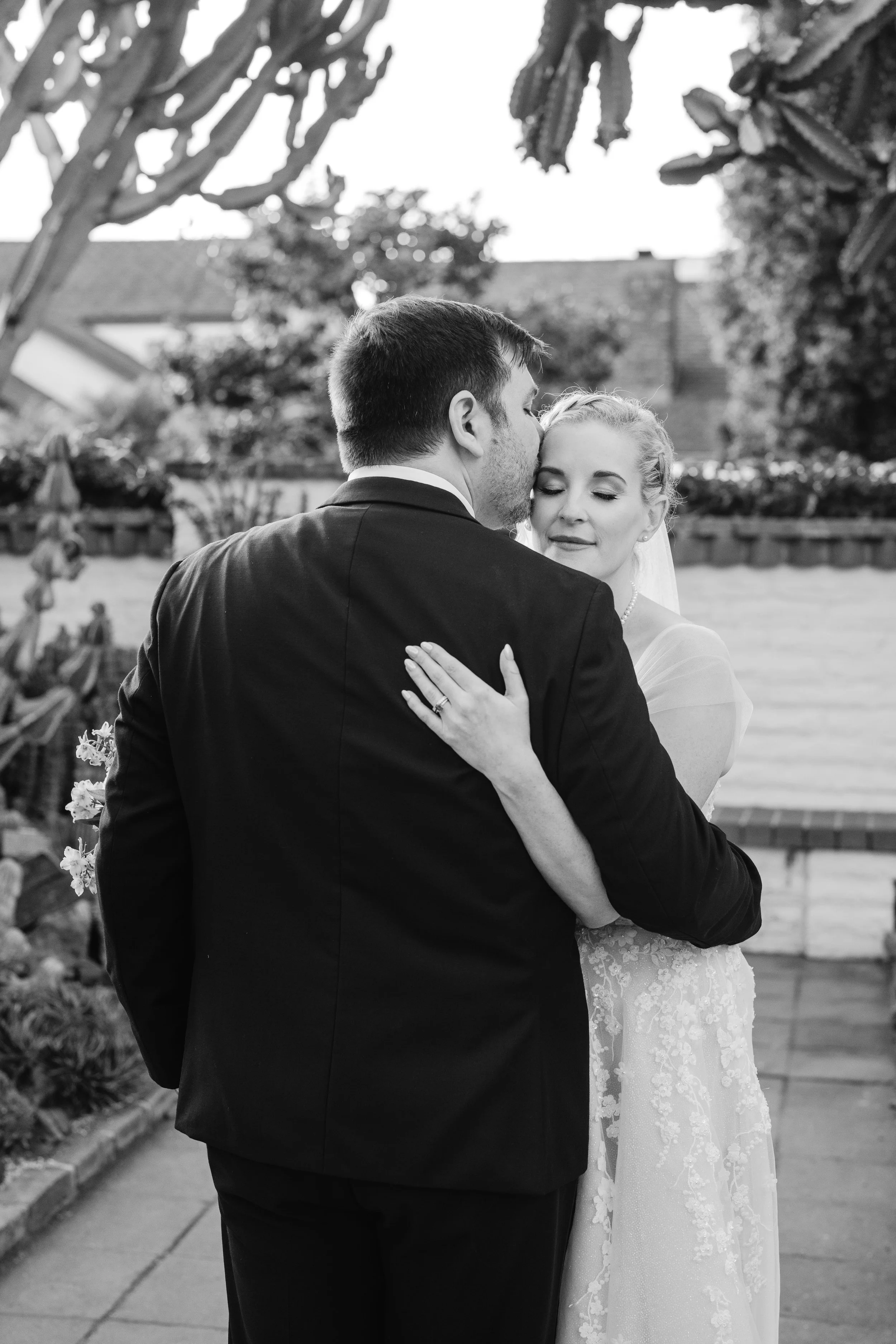 Black-and-white portrait of the groom kissing the bride’s forehead during an intimate embrace