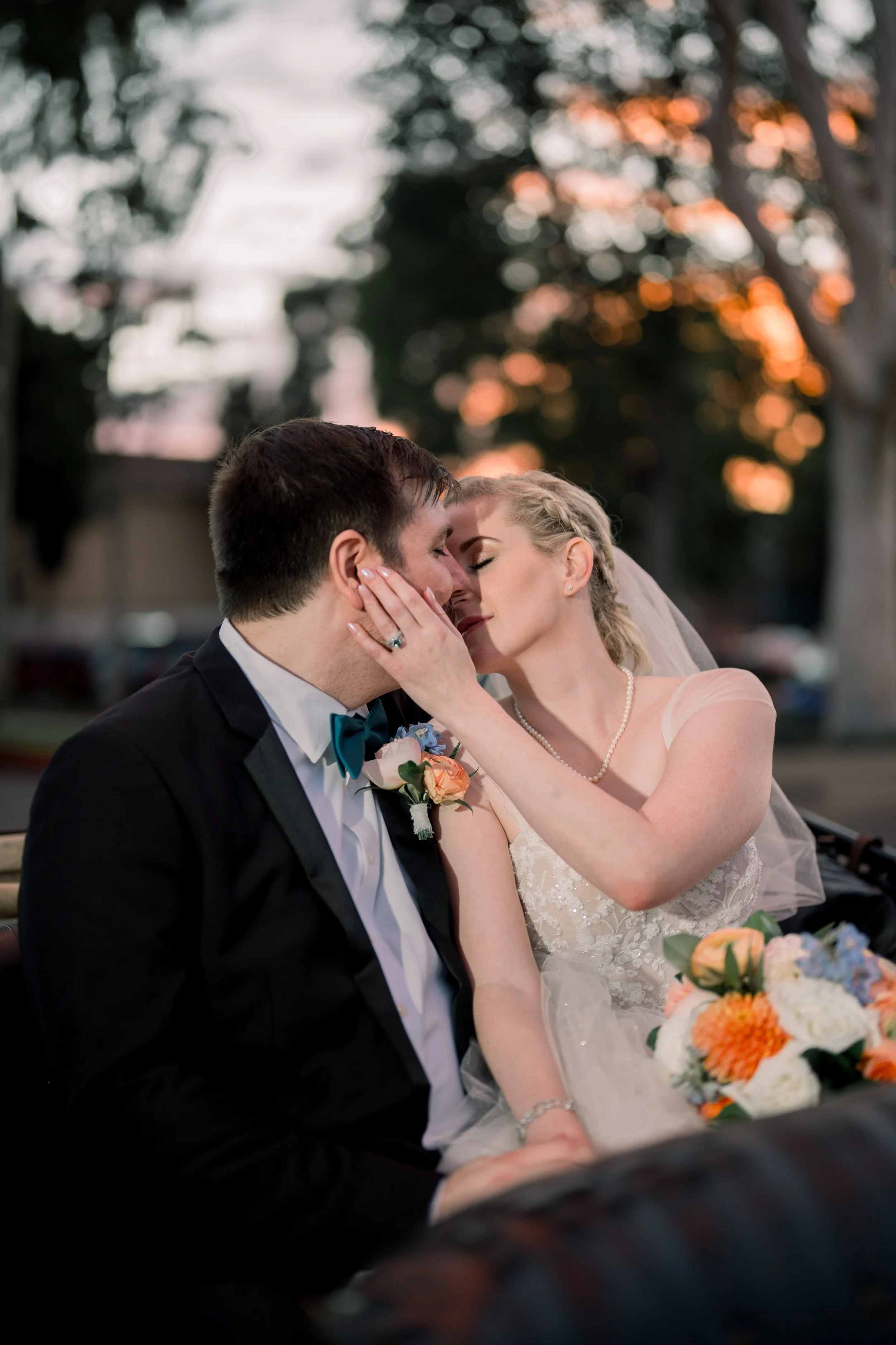 Bride gently holding the groom’s face as they lean in for a kiss while sitting in a vintage convertible at sunset