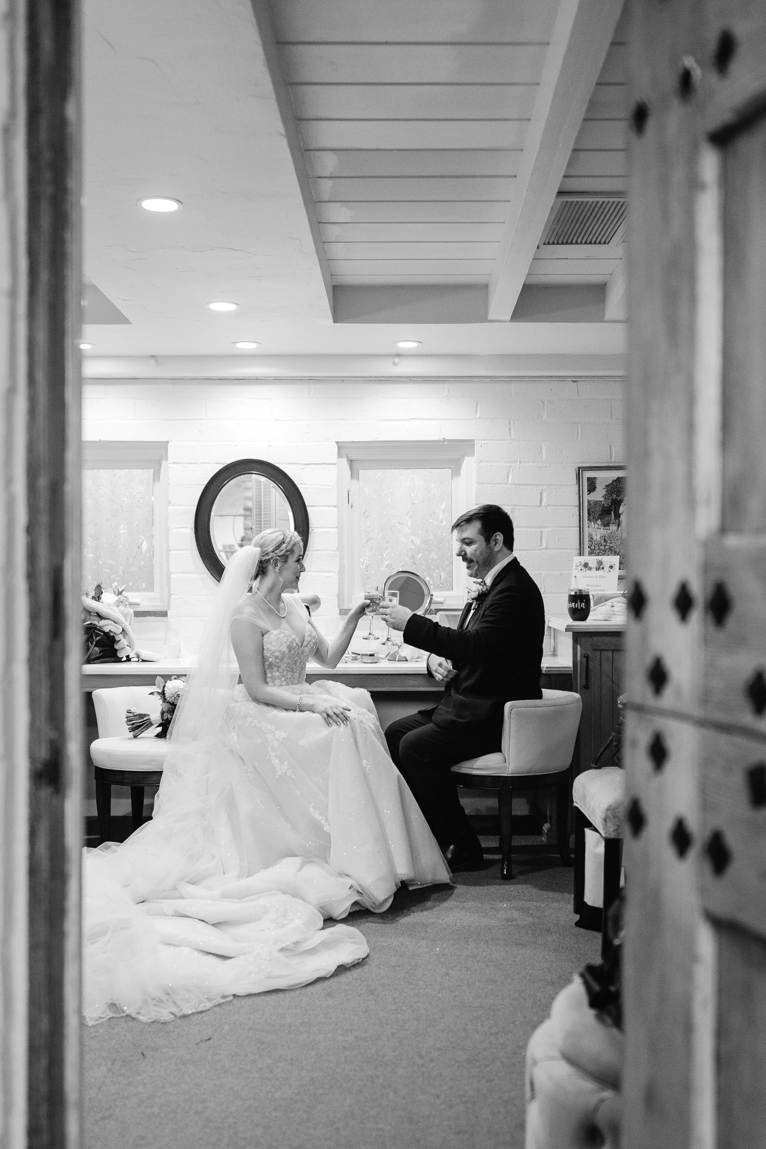 Black and white portrait of the bride and groom sharing a champagne toast together indoors after the ceremony