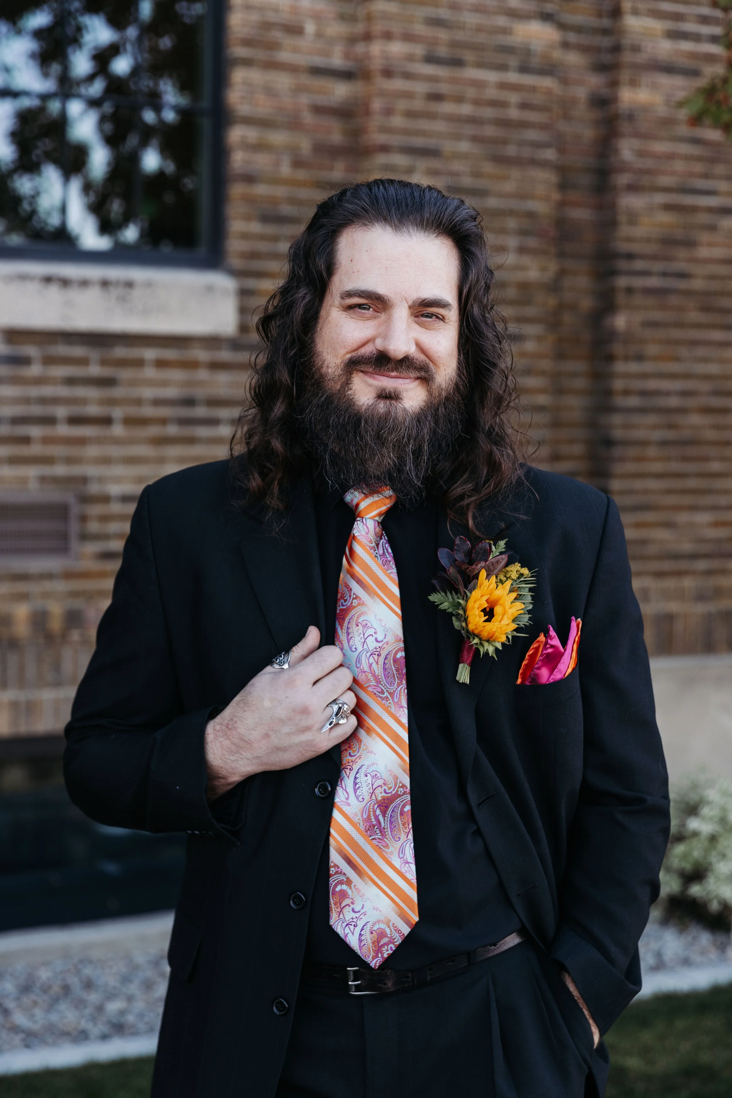 Groom portrait featuring a black suit, colorful patterned tie, sunflower boutonniere, and bold details that complemented the Día de los Muertos wedding theme.