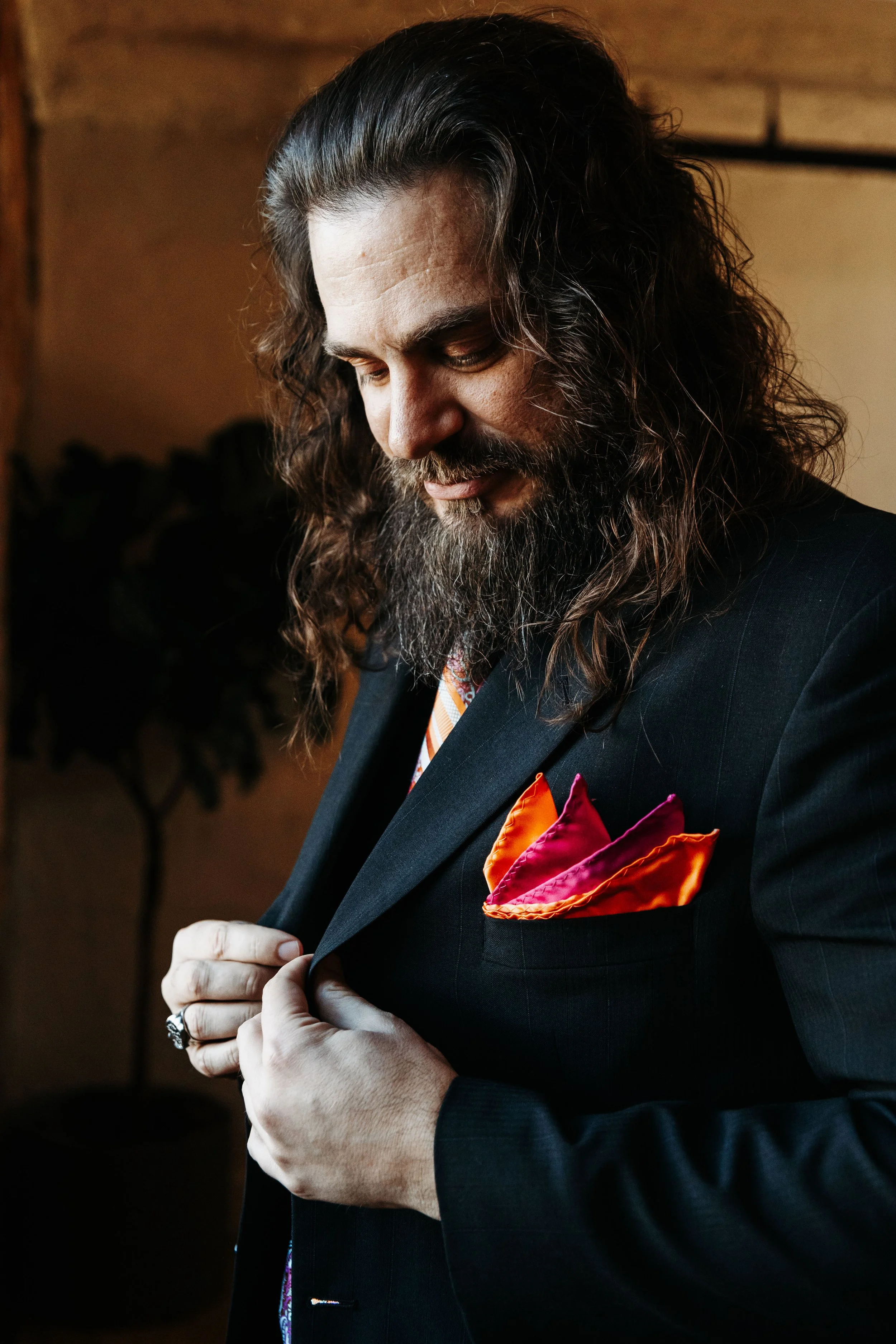 Portrait of a groom adjusting his suit jacket and vibrant pocket square while getting ready before the wedding ceremony.