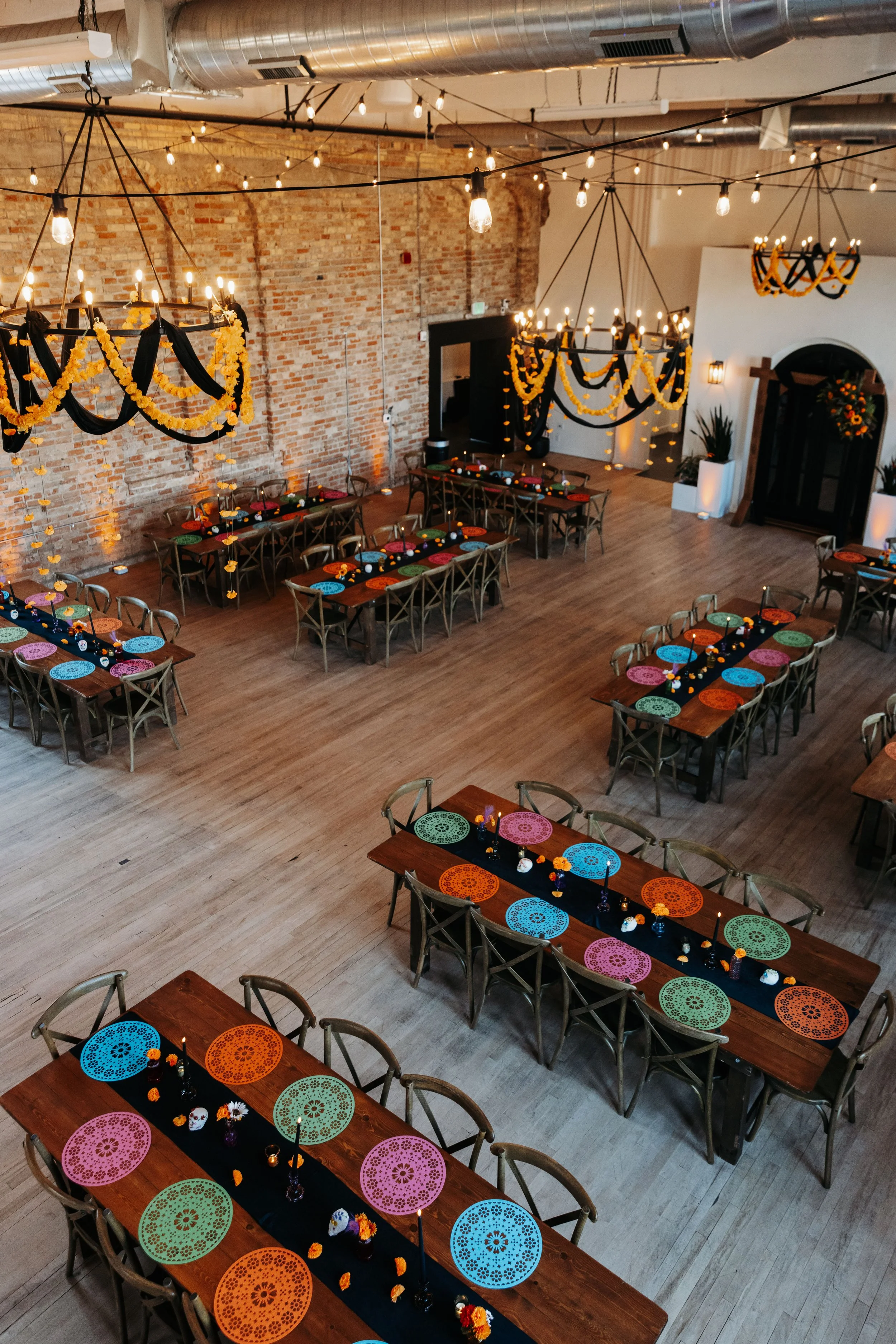 Reception setup inside Crescent Hall featuring colorful Día de los Muertos table décor, marigold garlands, black draping, and long banquet tables.