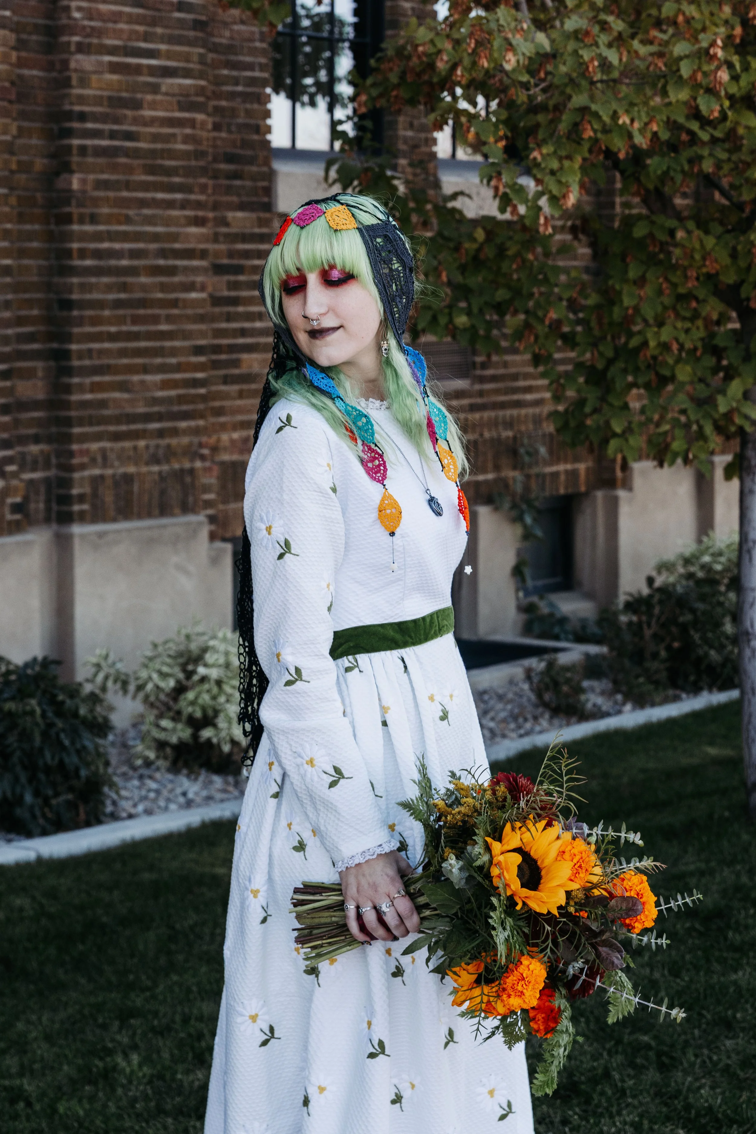Bride holding a bouquet of sunflowers and vibrant fall flowers while wearing colorful crocheted accessories during her wedding day portraits.