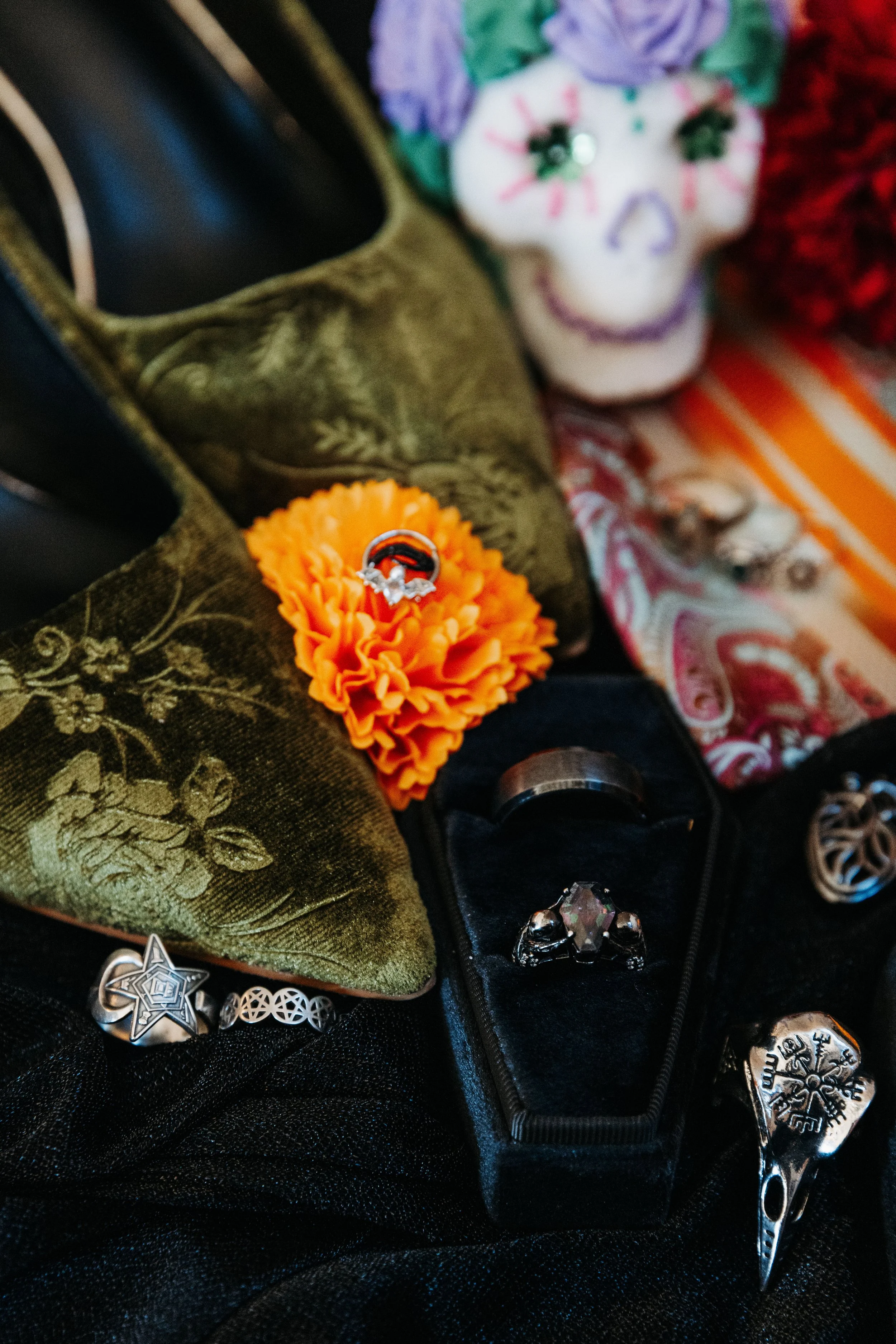 Wedding detail flat lay featuring rings, gothic-inspired accessories, embroidered shoes, and Día de los Muertos elements for a nontraditional wedding.