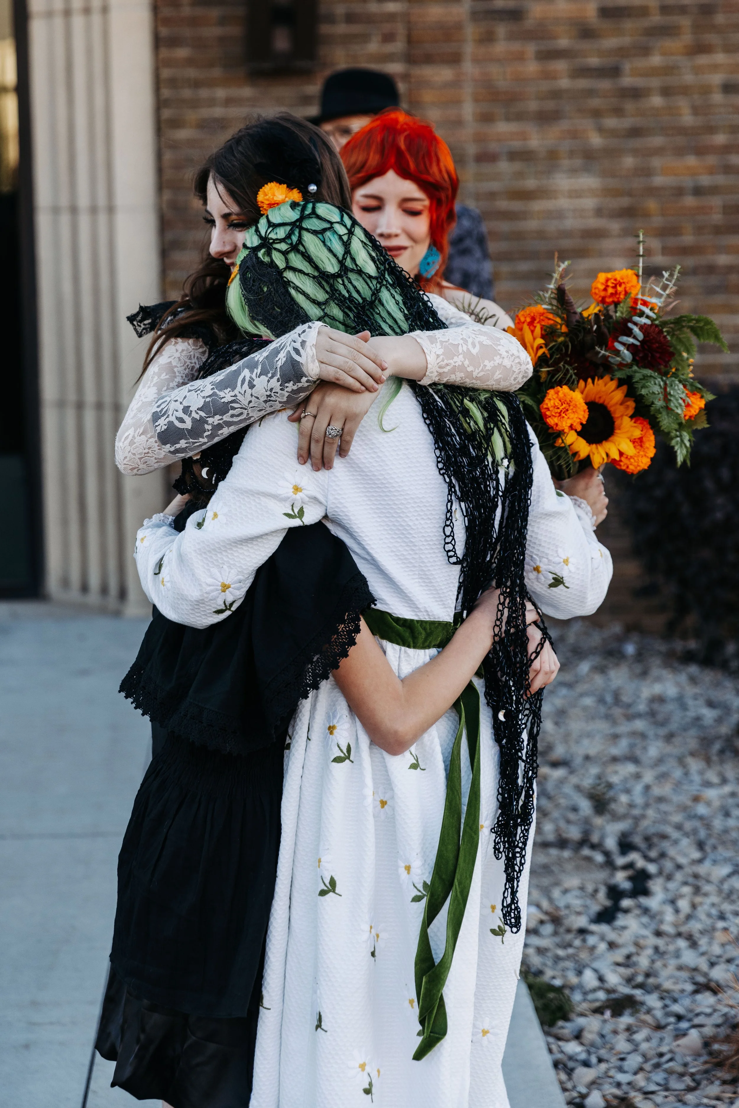 Bride shares a heartfelt group hug with family members after the wedding ceremony while holding a bouquet of sunflowers and seasonal blooms.