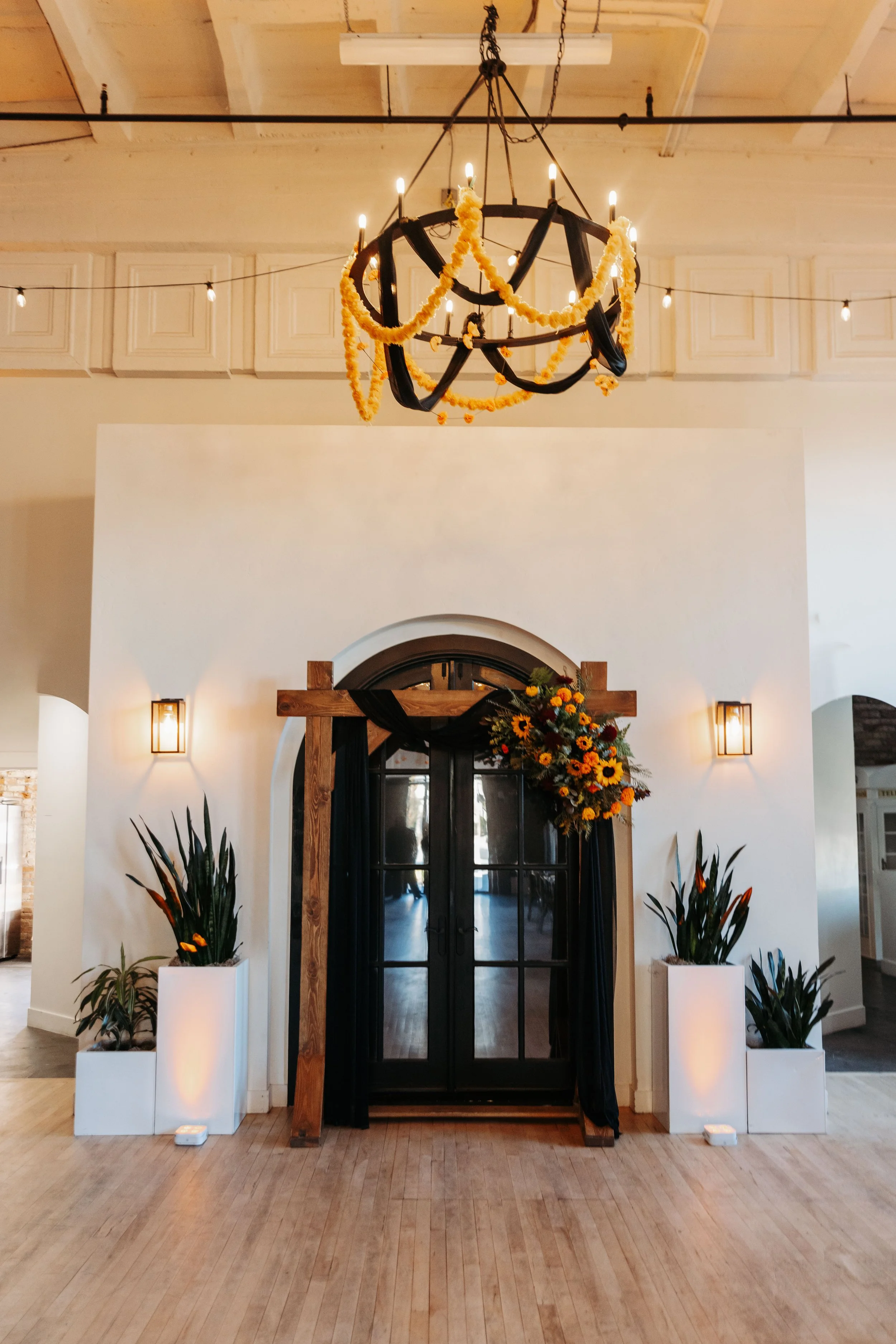 Ceremony backdrop at Crescent Hall in Sandy, Utah featuring a wooden arch, black draping, marigold florals, and Día de los Muertos-inspired wedding design.