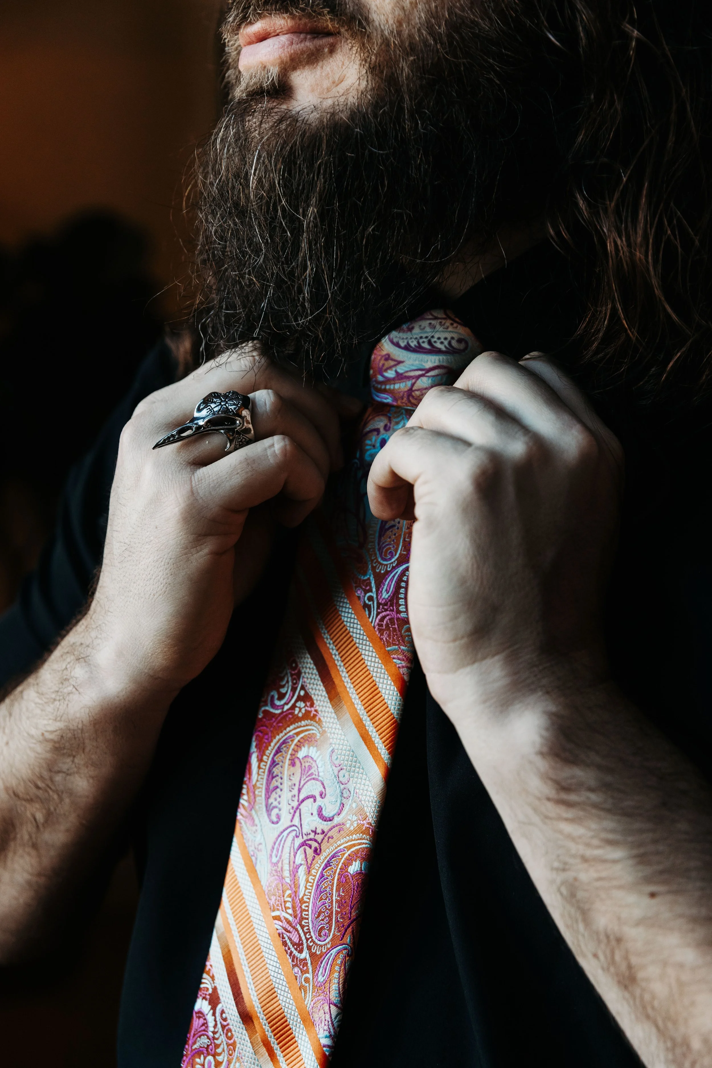 Close-up of the groom adjusting a colorful paisley necktie, highlighting personal style details and wedding attire accessories.