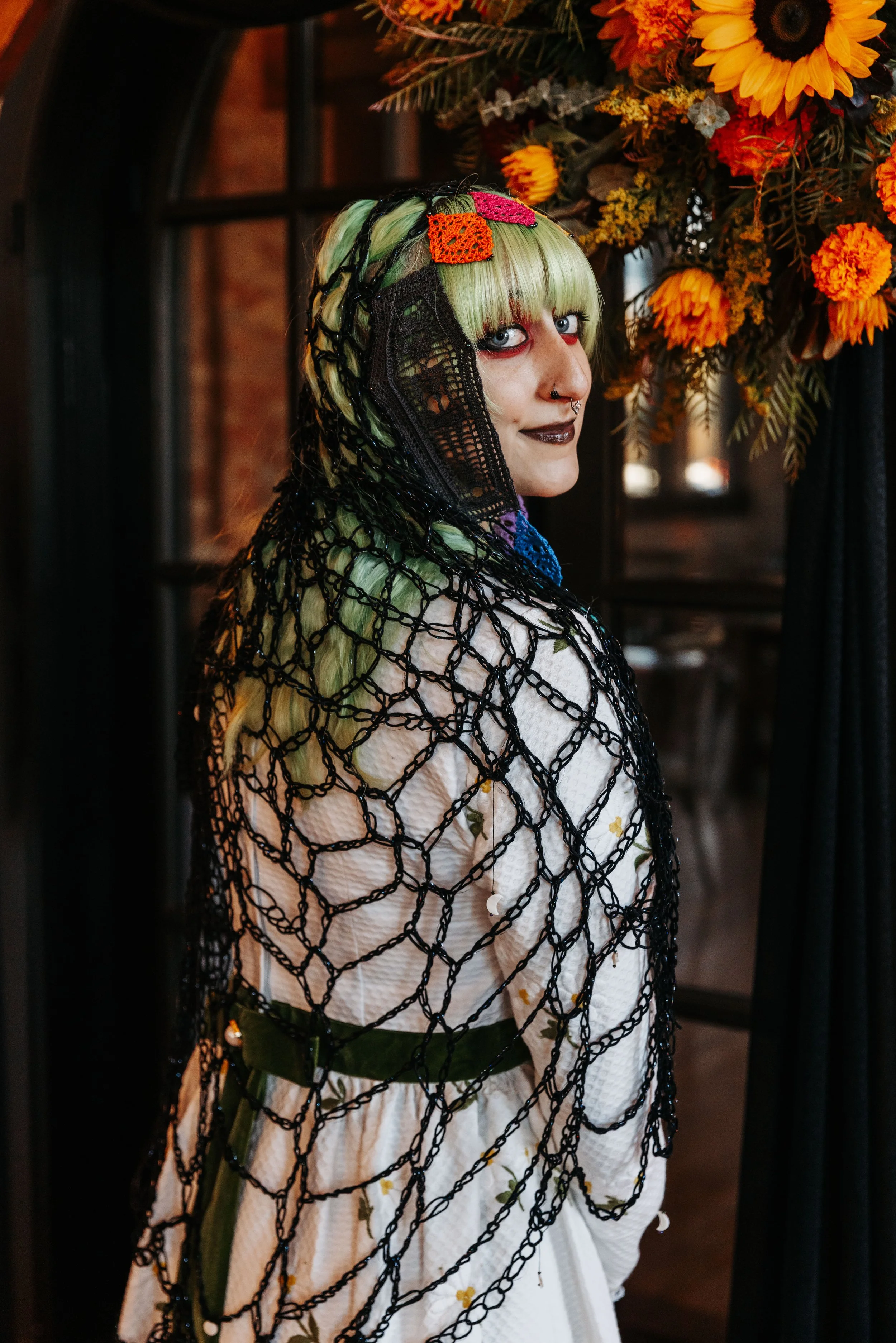 Bride wearing a custom crocheted veil and vintage-inspired wedding dress beneath vibrant floral arrangements during a Día de los Muertos wedding.