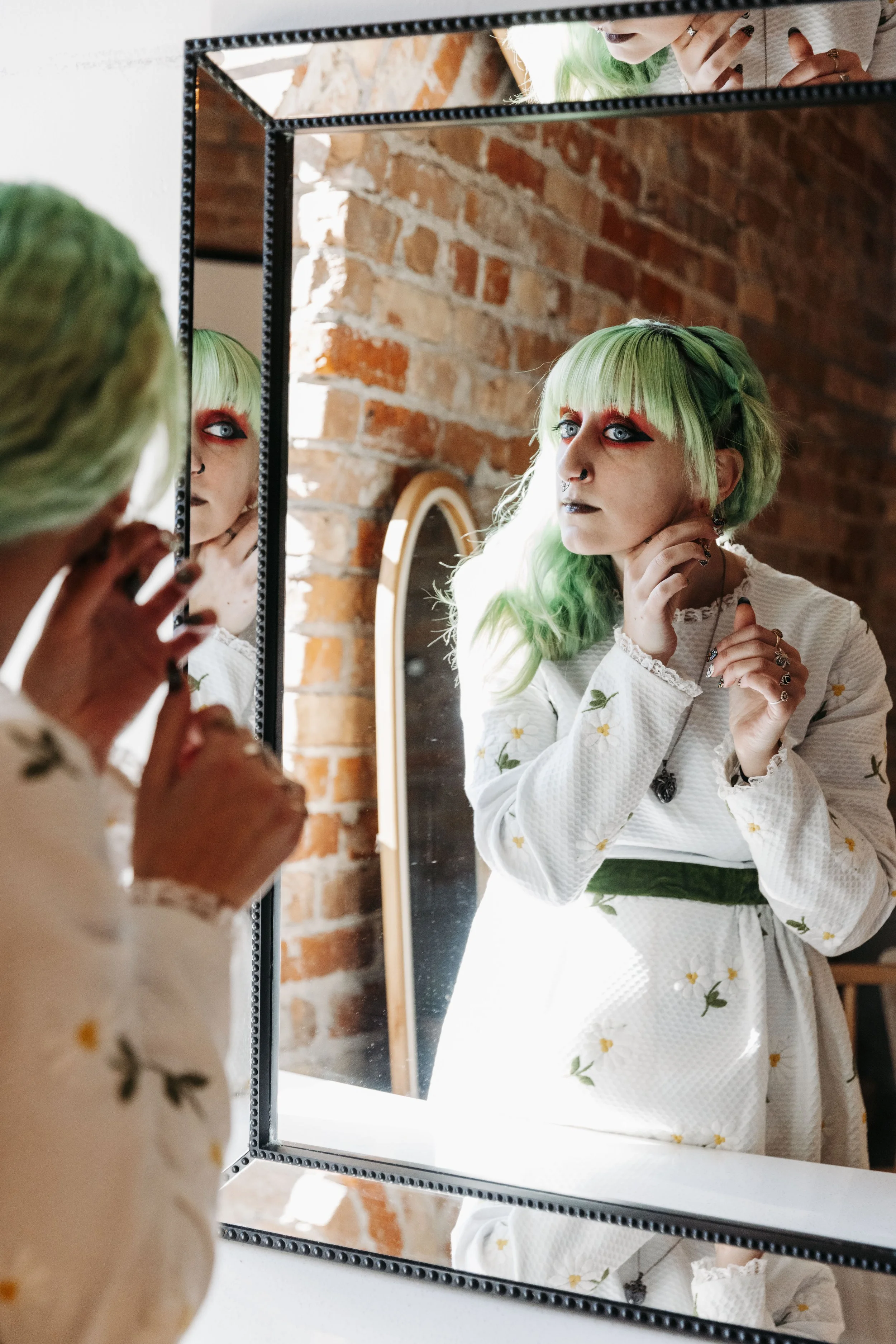 Bride adjusts her jewelry while looking into a mirror during wedding preparations, showcasing her unique bridal style and makeup.