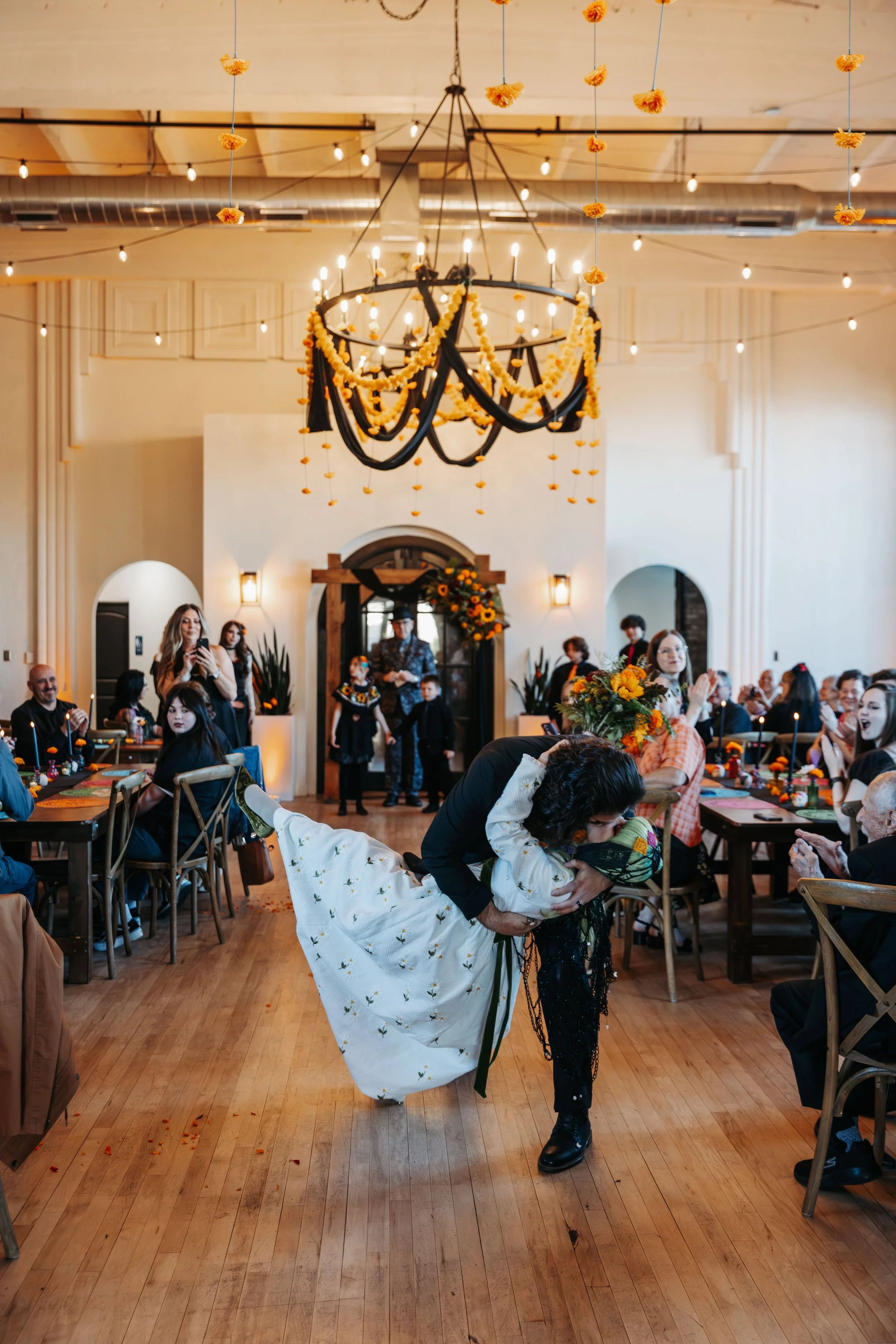 Groom dips the bride for a dramatic kiss in the center of the reception space while guests applaud and celebrate around them.