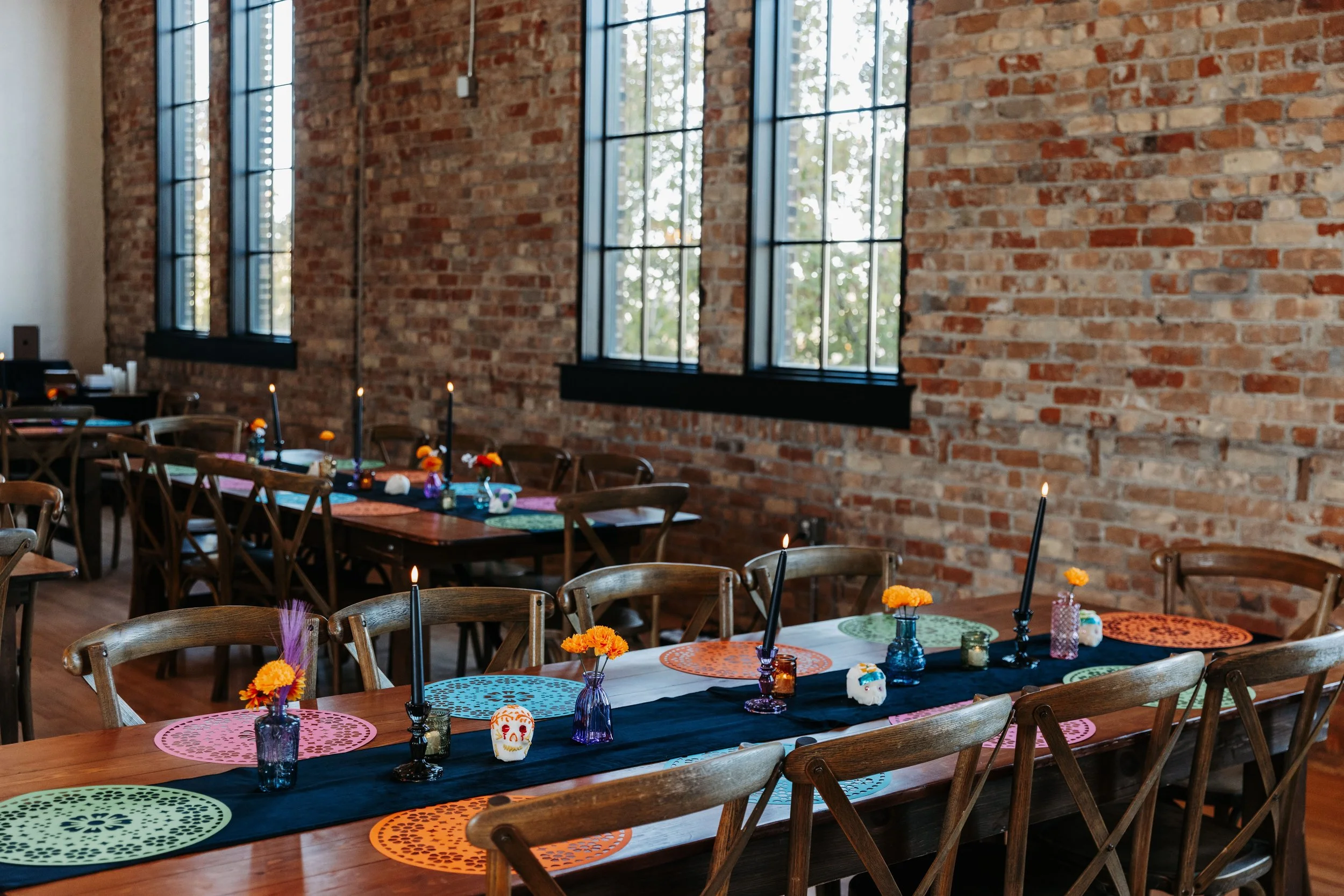 Reception tables set inside Crescent Hall in Sandy, Utah, featuring colorful Día de los Muertos wedding decor, marigold accents, and black candle centerpieces.