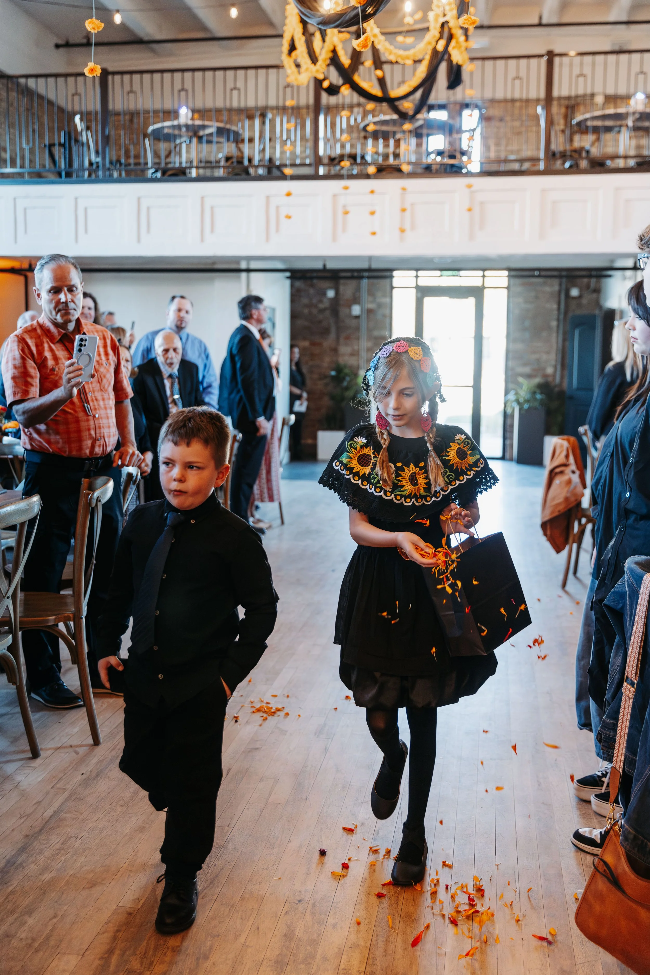 Flower girl and ring bearer walk down the aisle carrying petals during a wedding ceremony at Crescent Hall, with guests watching from their seats.