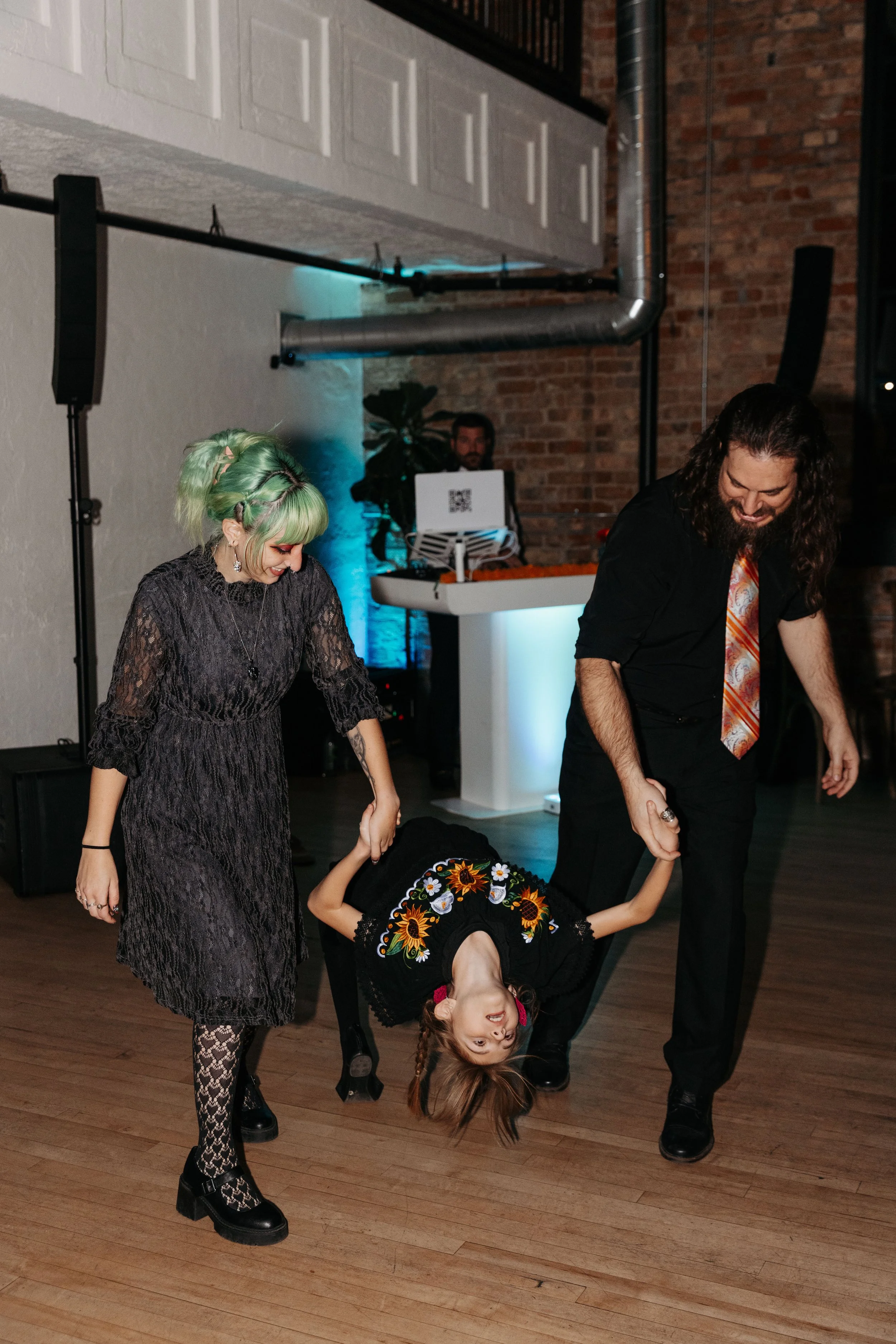 A couple dances with a young family member during the reception, creating a playful and memorable moment on the dance floor at their Día de los Muertos-inspired wedding.