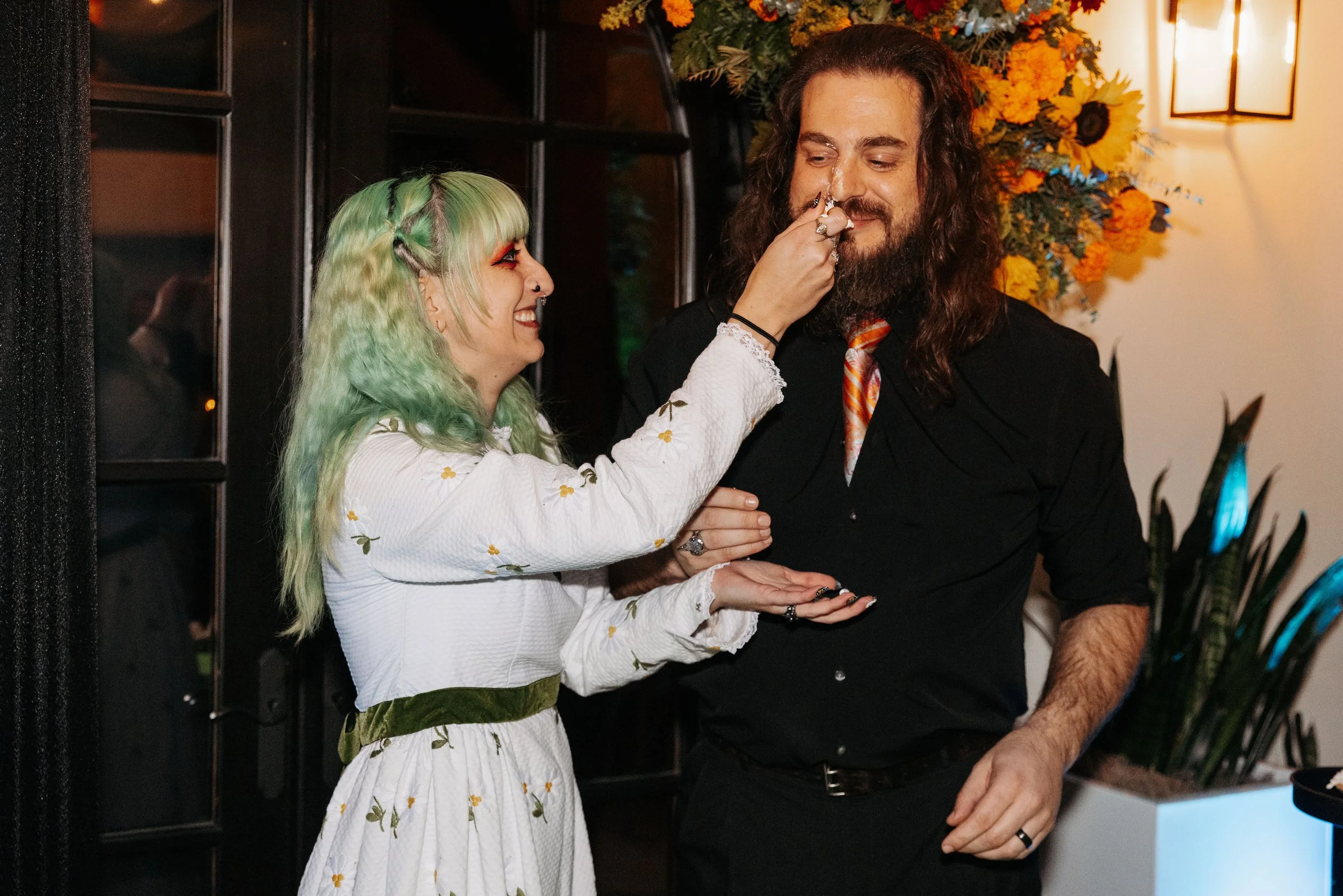 Bride playfully feeds the groom a bite of wedding dessert during the reception while surrounded by seasonal floral décor.