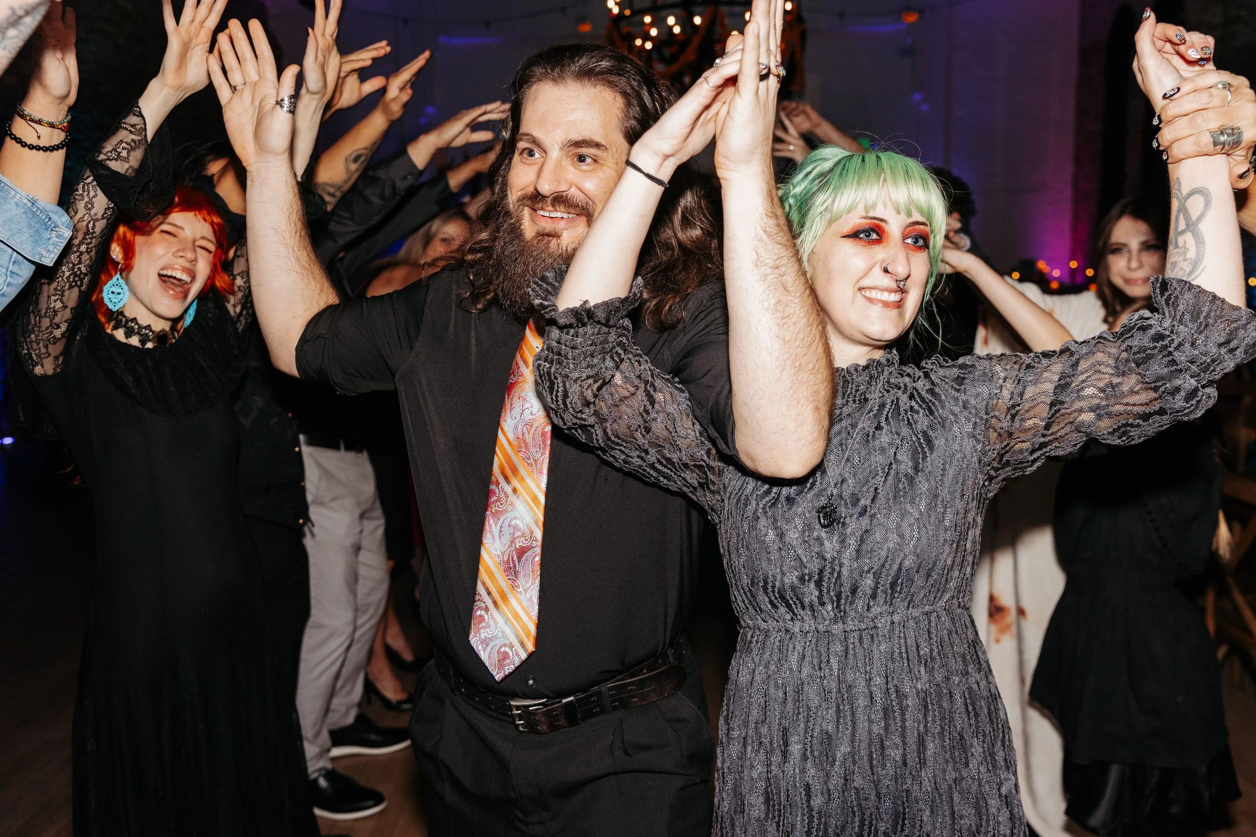 Newlyweds celebrate on a crowded dance floor with family and friends, raising their hands and enjoying the wedding reception festivities.