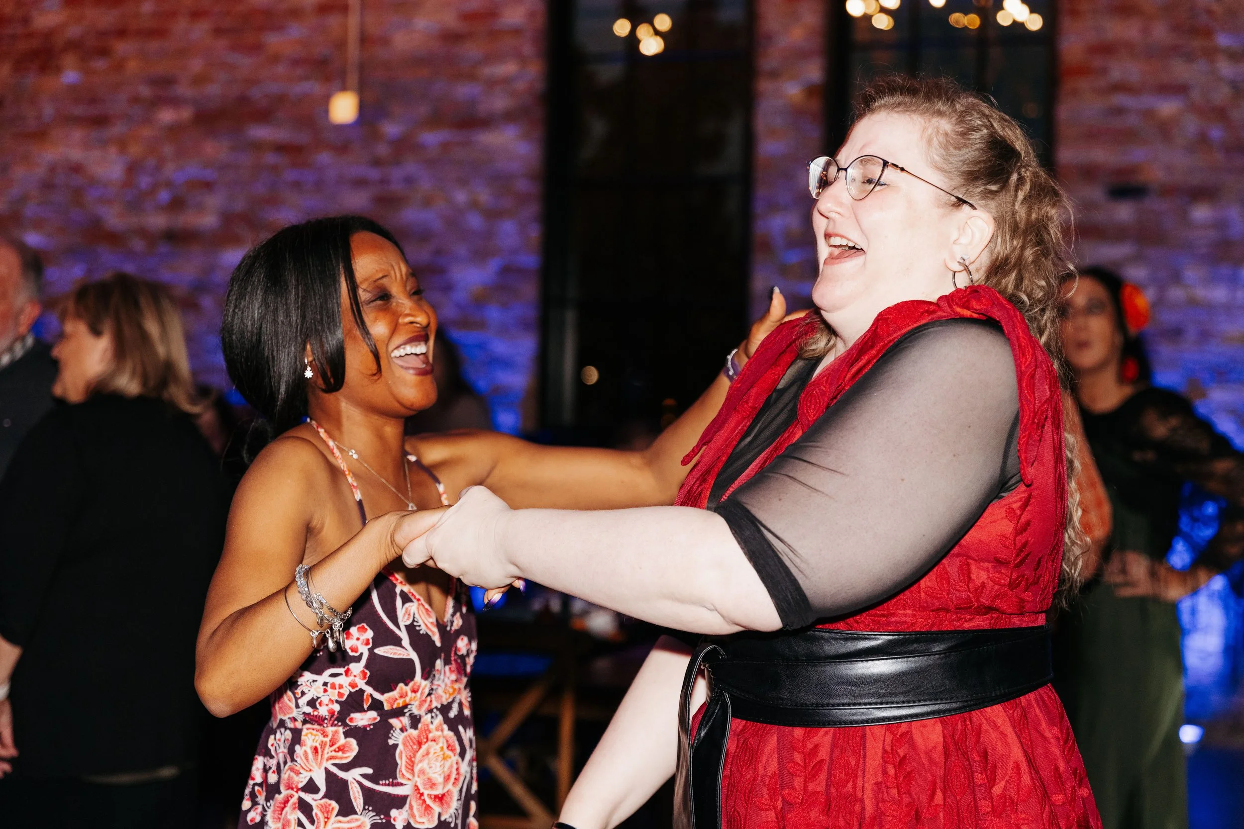 Wedding guests laugh and dance together on the reception dance floor during an energetic evening celebration.