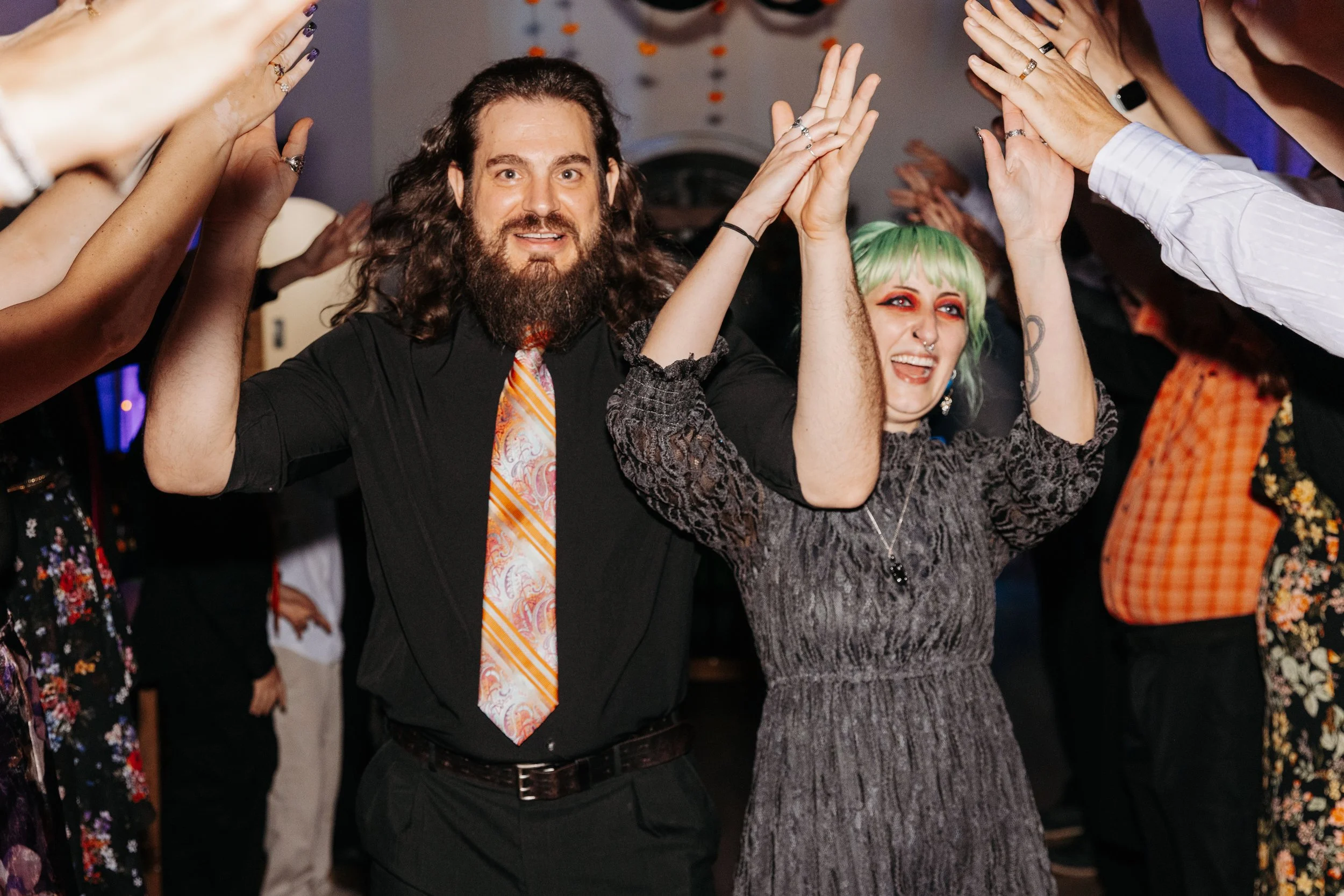 Newlyweds enter their wedding reception holding hands while guests cheer and raise their arms around them.