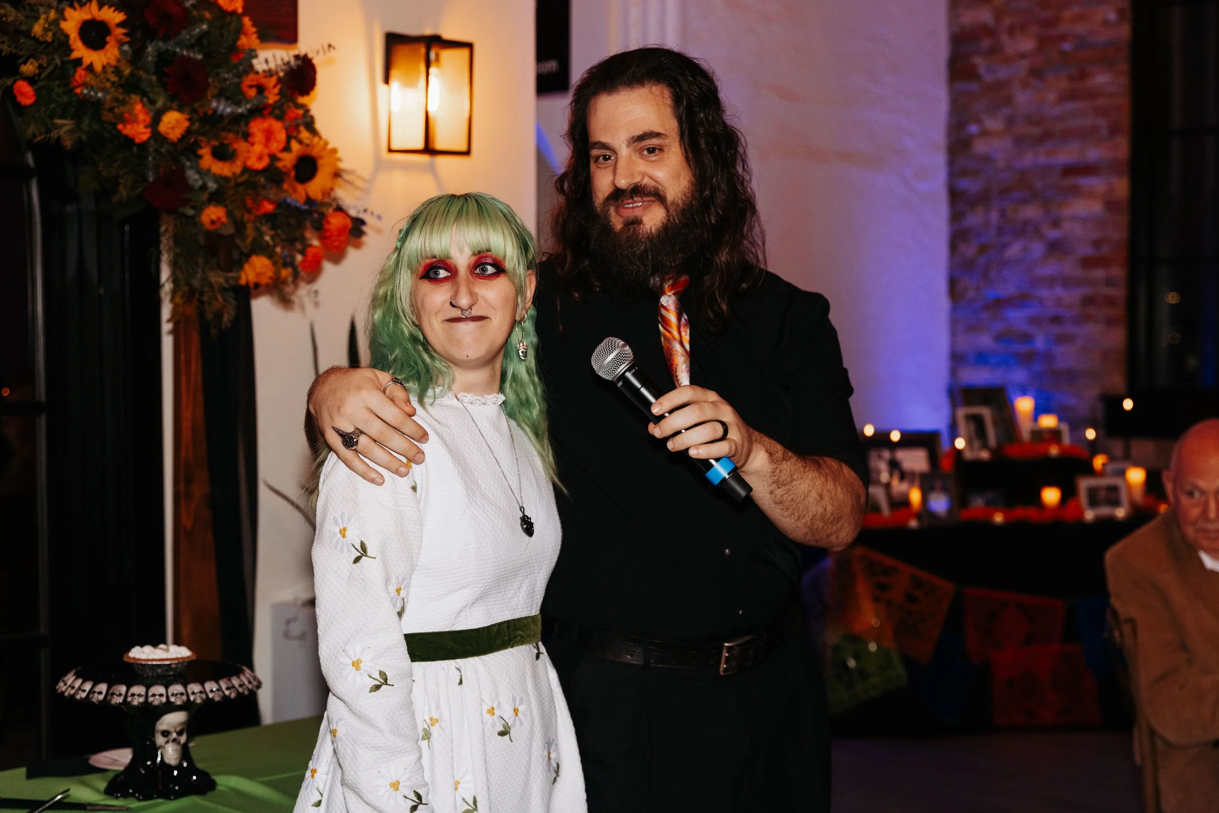Groom wraps an arm around the bride while speaking into a microphone during a heartfelt wedding reception toast.