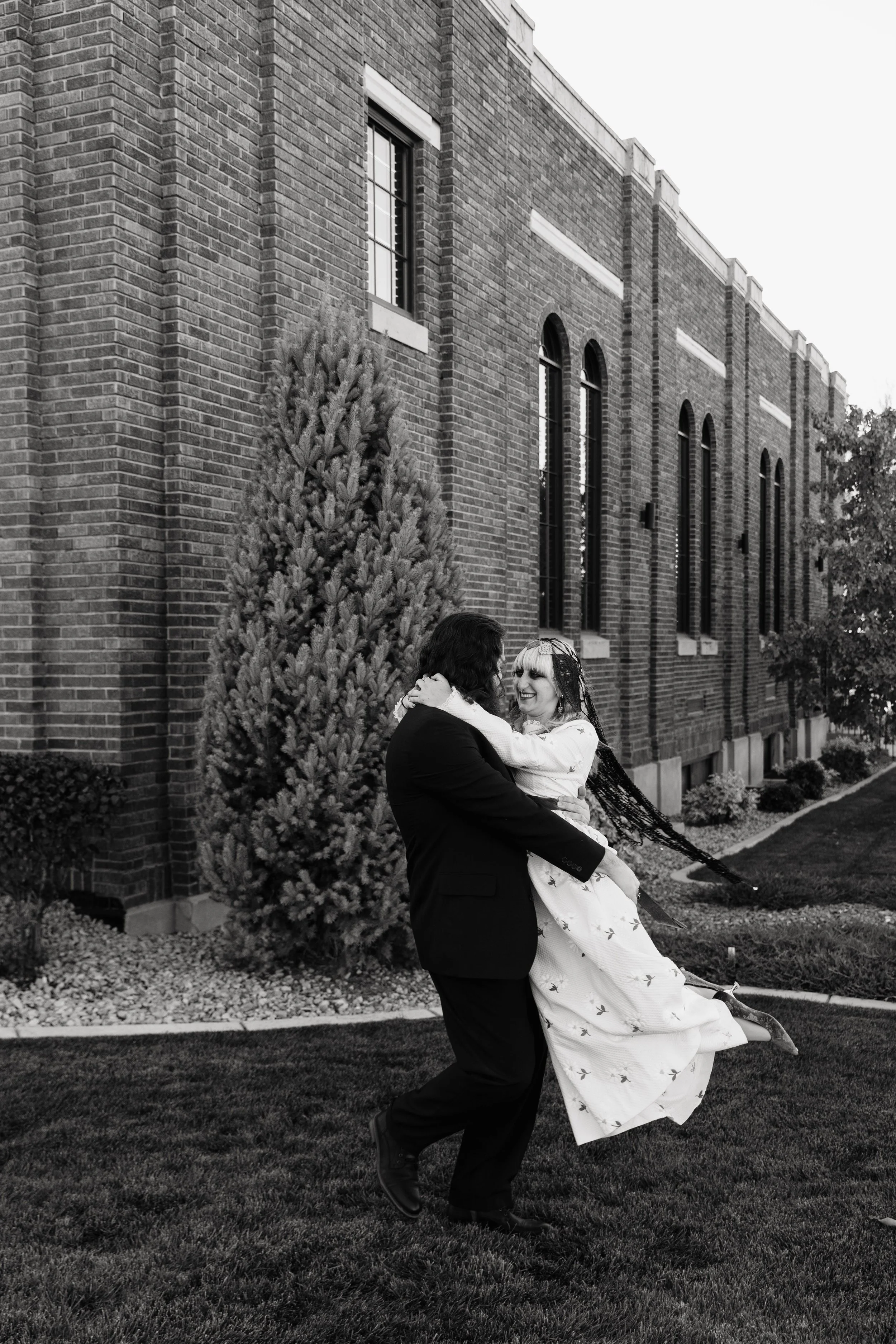 Bride laughs as she is lifted and spun by her partner outside Crescent Hall, capturing a joyful and candid moment during their alternative wedding portraits.