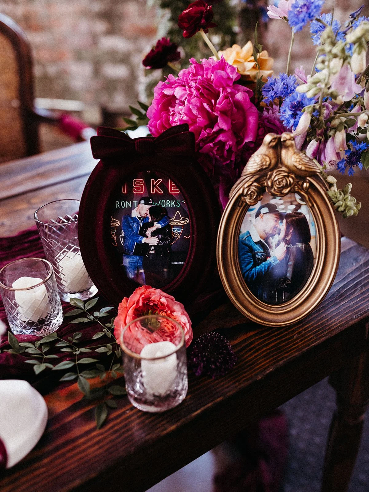 Framed photos of the couple displayed alongside colorful flowers, candles, and burgundy wedding décor on a reception table.