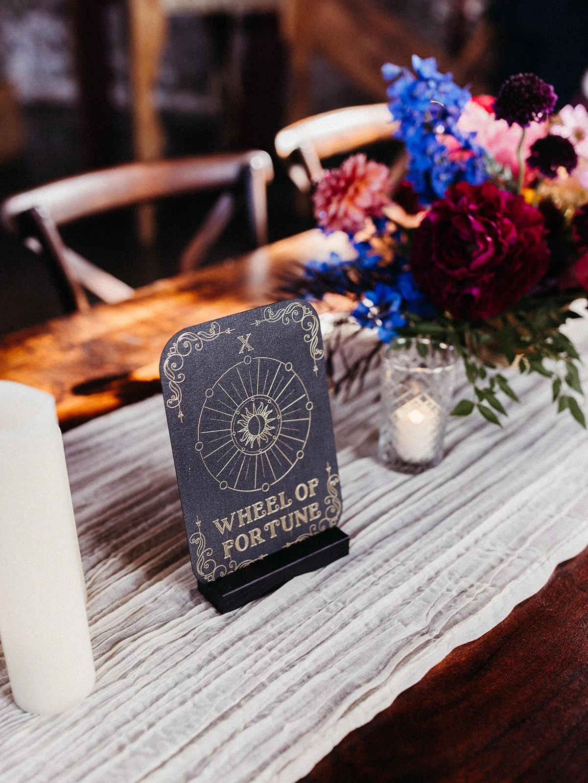Tarot-inspired "Wheel of Fortune" table marker displayed on a reception table with candles, colorful florals, and textured linen décor.