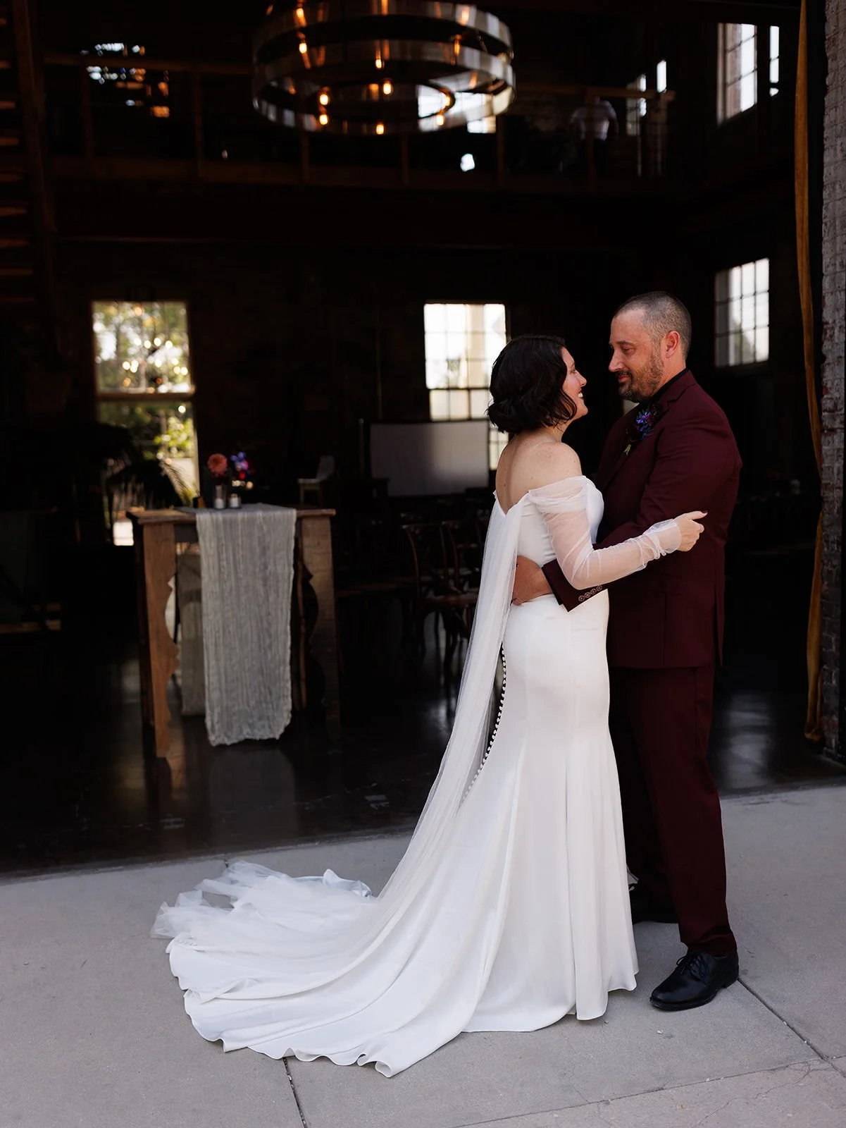 Bride and groom embrace during their first look outside a historic industrial wedding venue, showcasing modern wedding fashion and an intimate pre-ceremony moment.