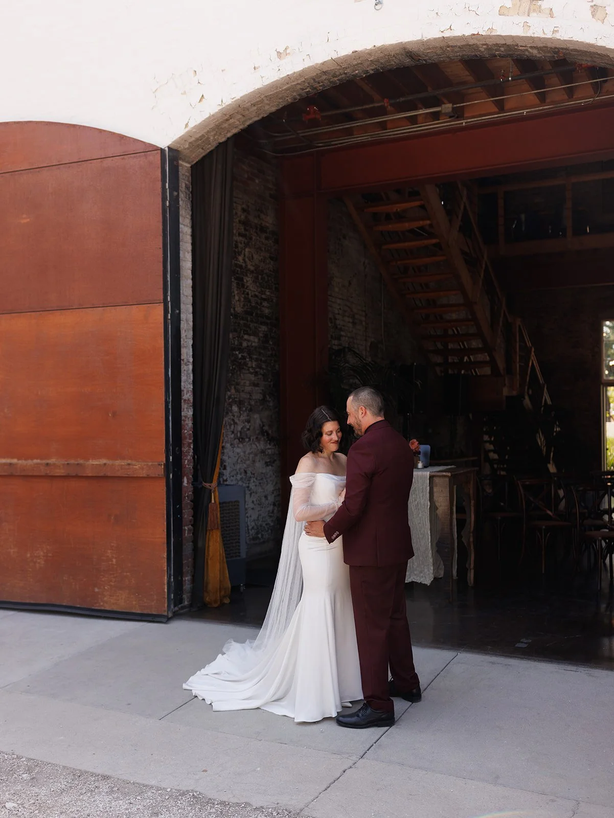 Bride and groom share a quiet embrace in front of large industrial venue doors, highlighting a modern and intimate wedding day portrait.