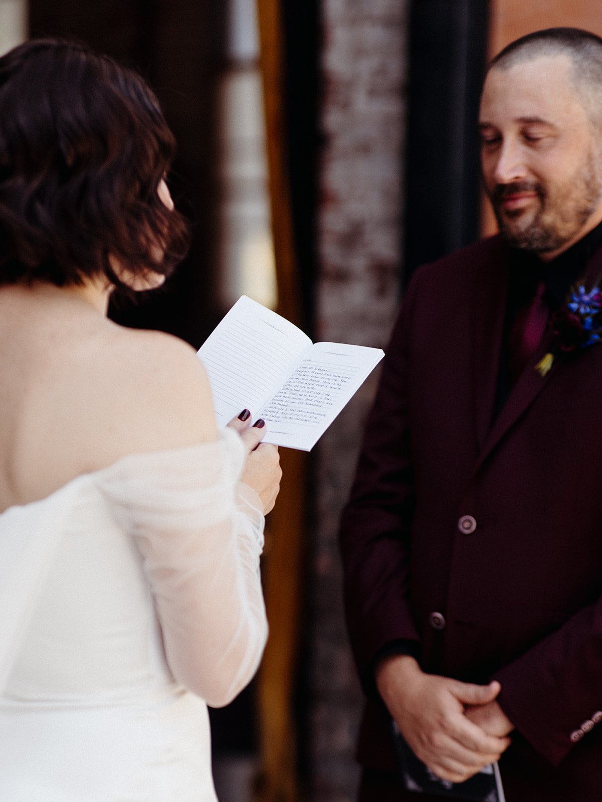 Bride reads a handwritten letter from her vow book while the groom listens attentively during an intimate first look before their wedding ceremony.