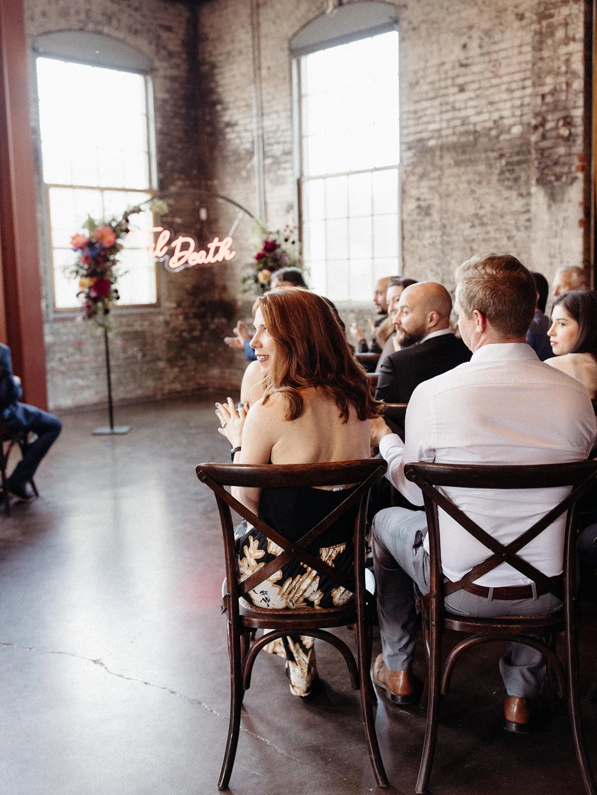 Guests seated down ceremony aisle before exchanging vows, celebrating their marriage with joyful smiles and colorful floral arrangements in the background