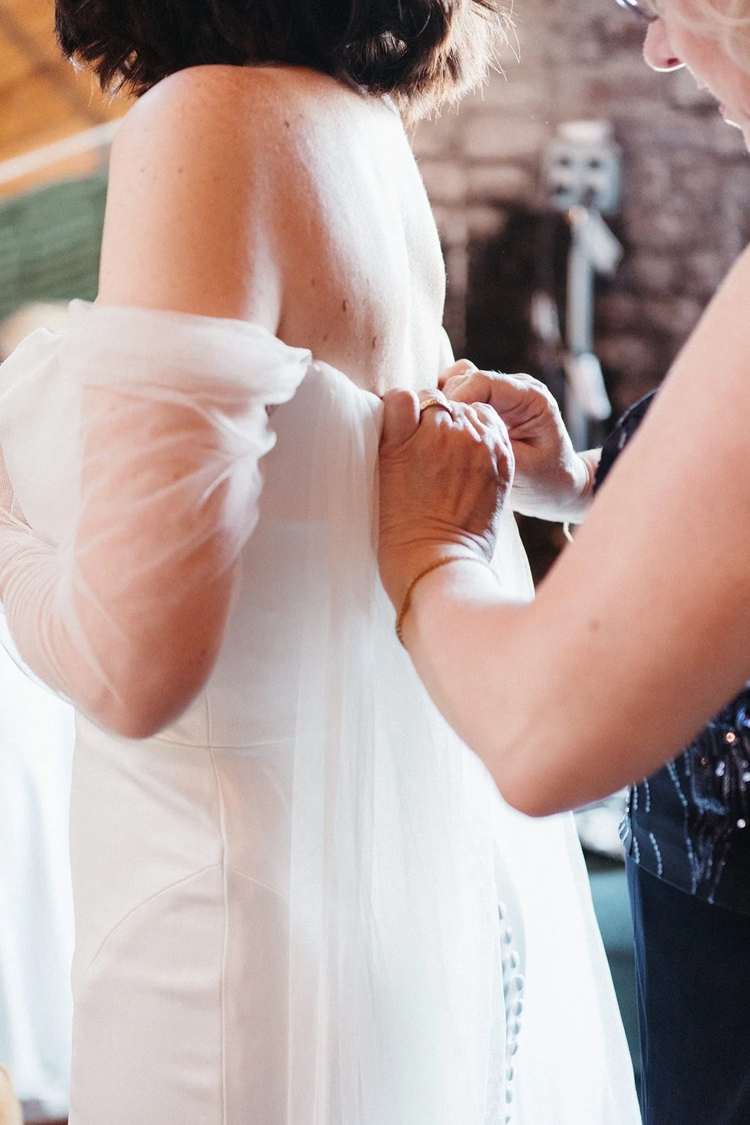 A family member fastens the back of the bride’s wedding dress during final preparations before the ceremony.