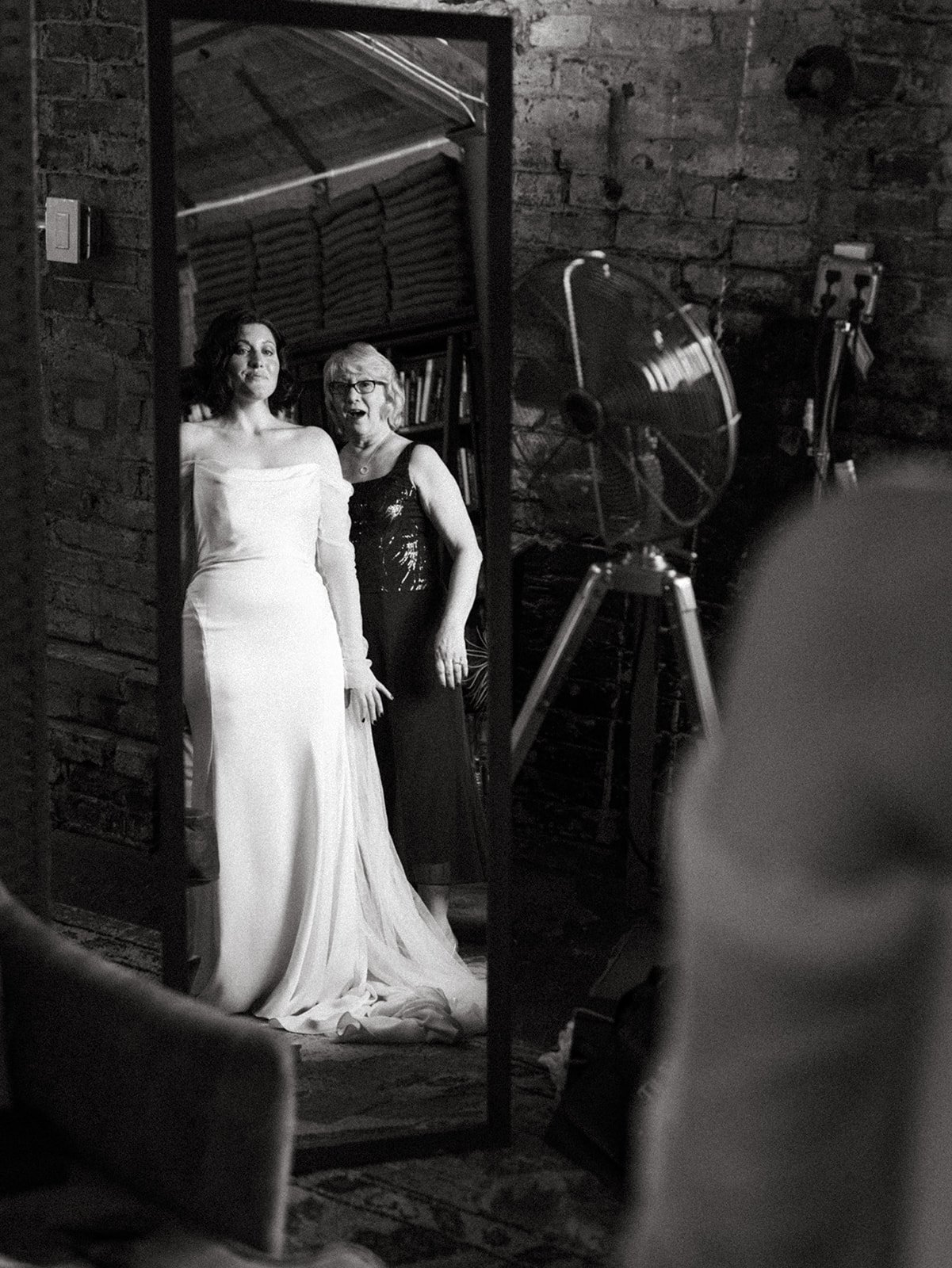 Bride and her mother share an emotional moment reflected in a mirror while getting ready before the wedding ceremony.