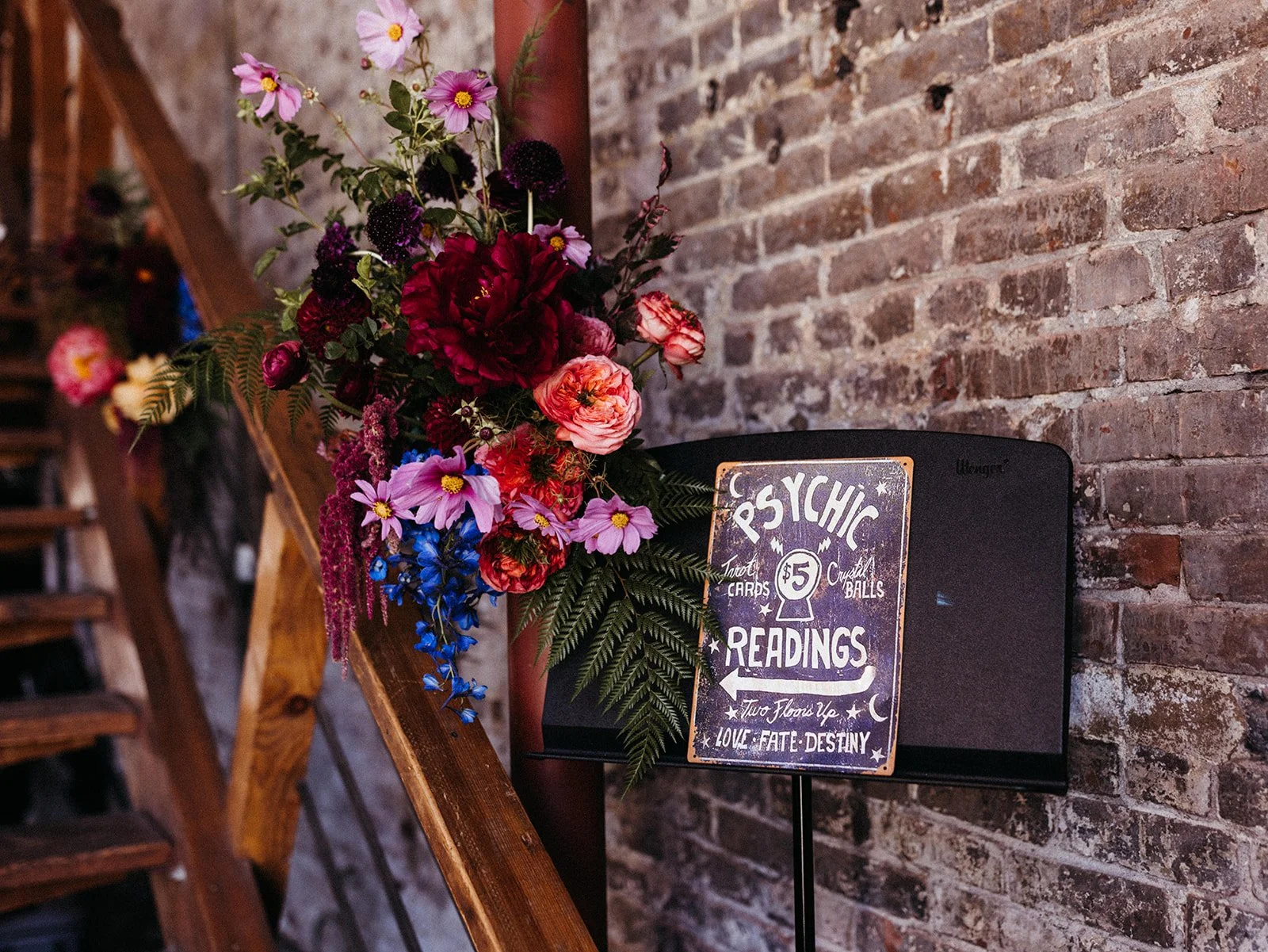 Colorful floral arrangement and vintage-style psychic readings sign displayed against exposed brick walls at a themed wedding reception.