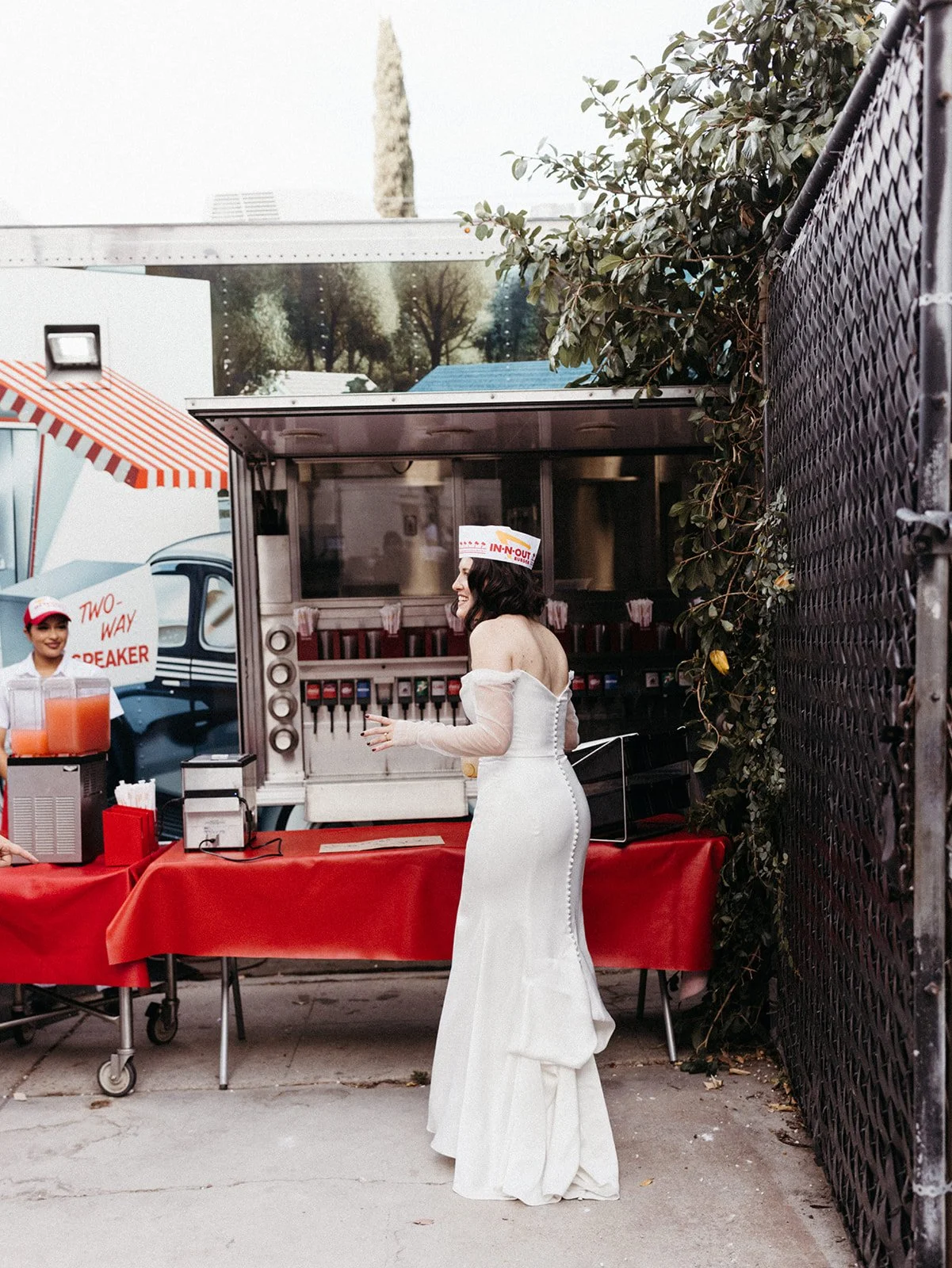 Bride wearing an In-N-Out paper hat visits a late-night burger station during the wedding reception, adding a fun and personalized guest experience.