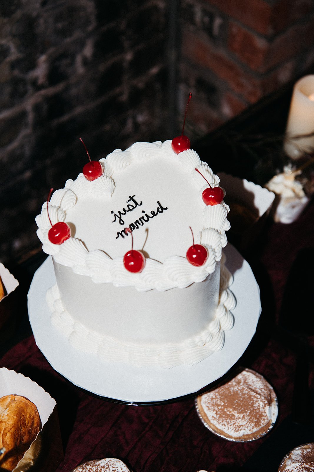 Vintage-inspired white wedding cake topped with bright red cherries on a dessert display table, blending playful design elements with an unconventional wedding aesthetic.