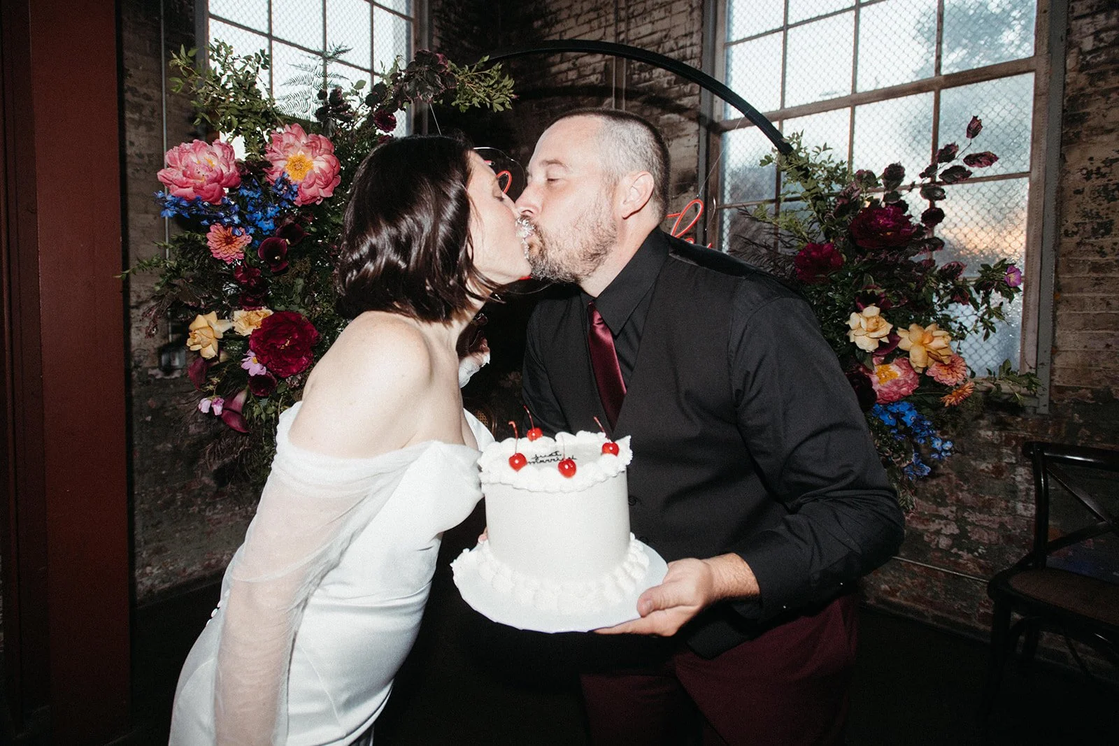 Bride and groom sharing a kiss during cake cutting at a personalized Friday the 13th wedding reception, surrounded by colorful florals and unique design details that reflect their vision and style.