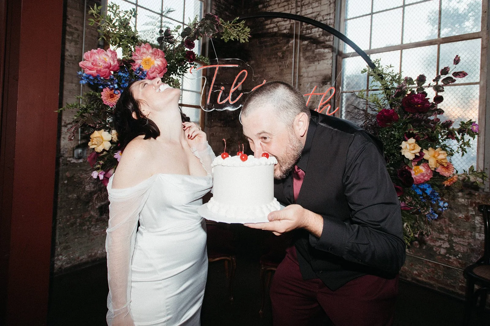 Bride and groom laughing during a playful cake-cutting moment at a personalized Friday the 13th wedding reception, showcasing an unconventional wedding celebration filled with personality.