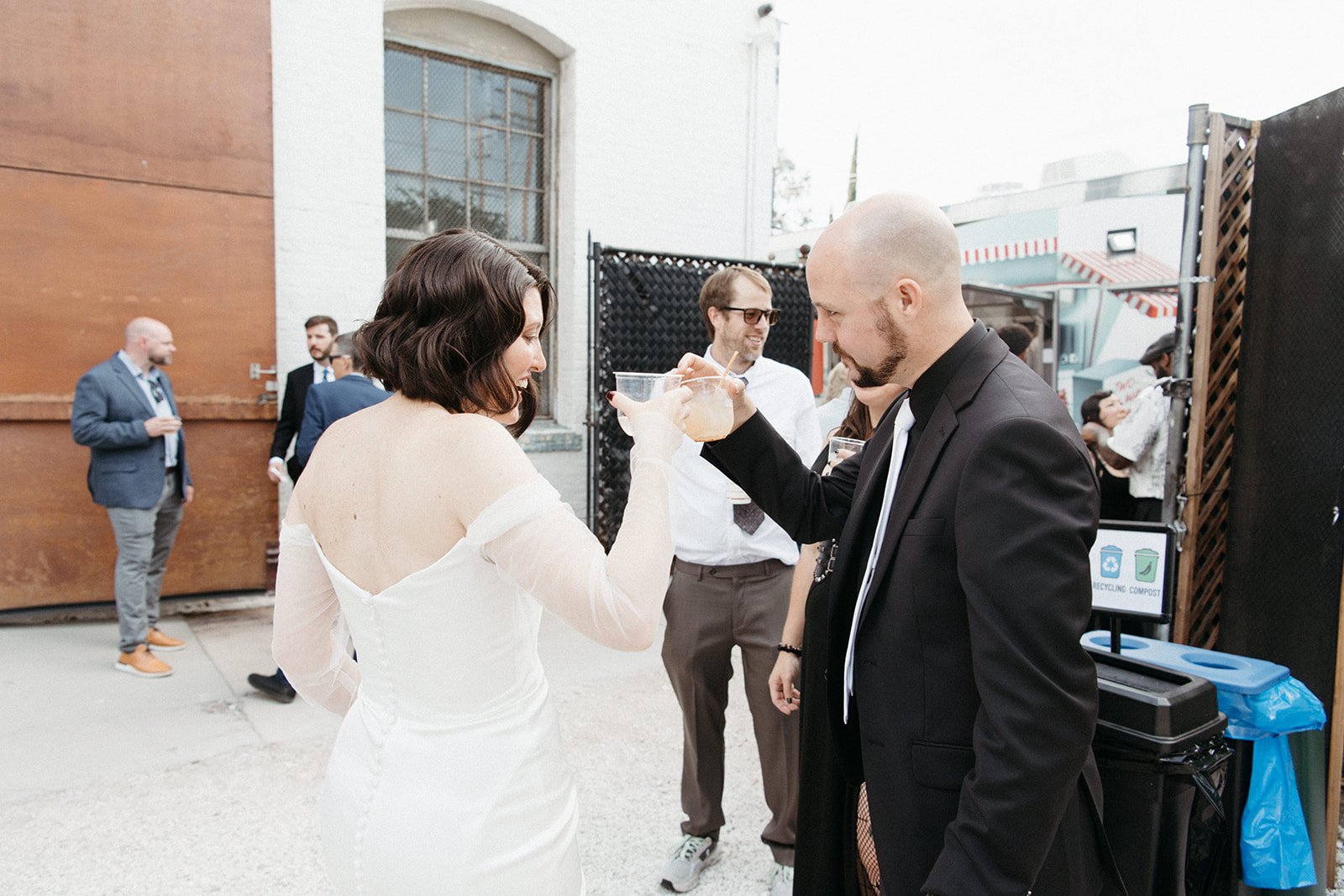 Bride shares a toast with wedding guests during cocktail hour near the outdoor reception space, celebrating with signature drinks and friends.