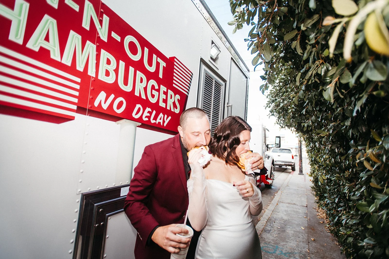 Bride and groom enjoy In-N-Out burgers together beside a food truck after their wedding ceremony, creating a fun and relaxed portrait.