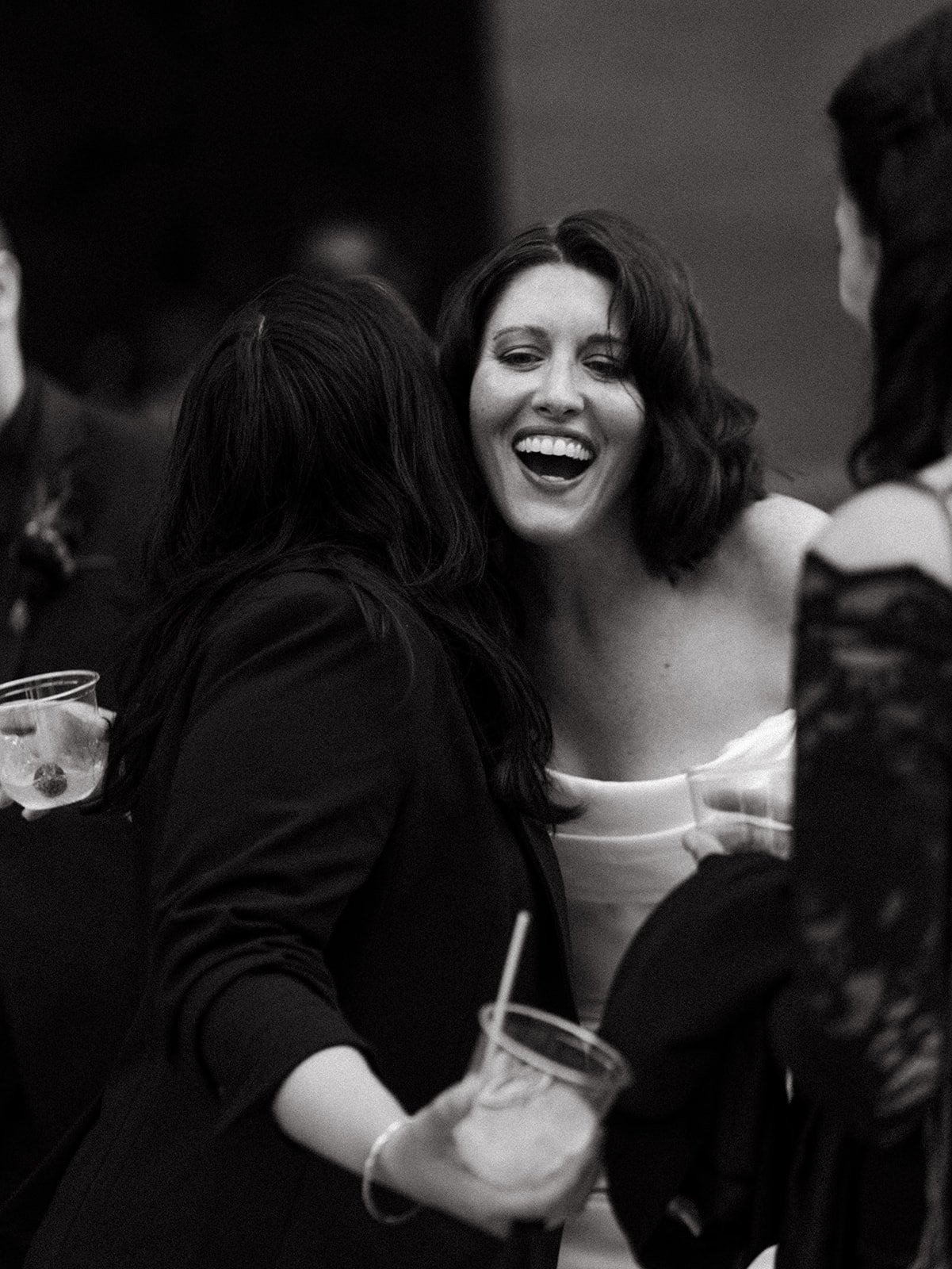 Bride smiles and chats with wedding guests during the reception while holding a drink inside a moody industrial wedding venue.