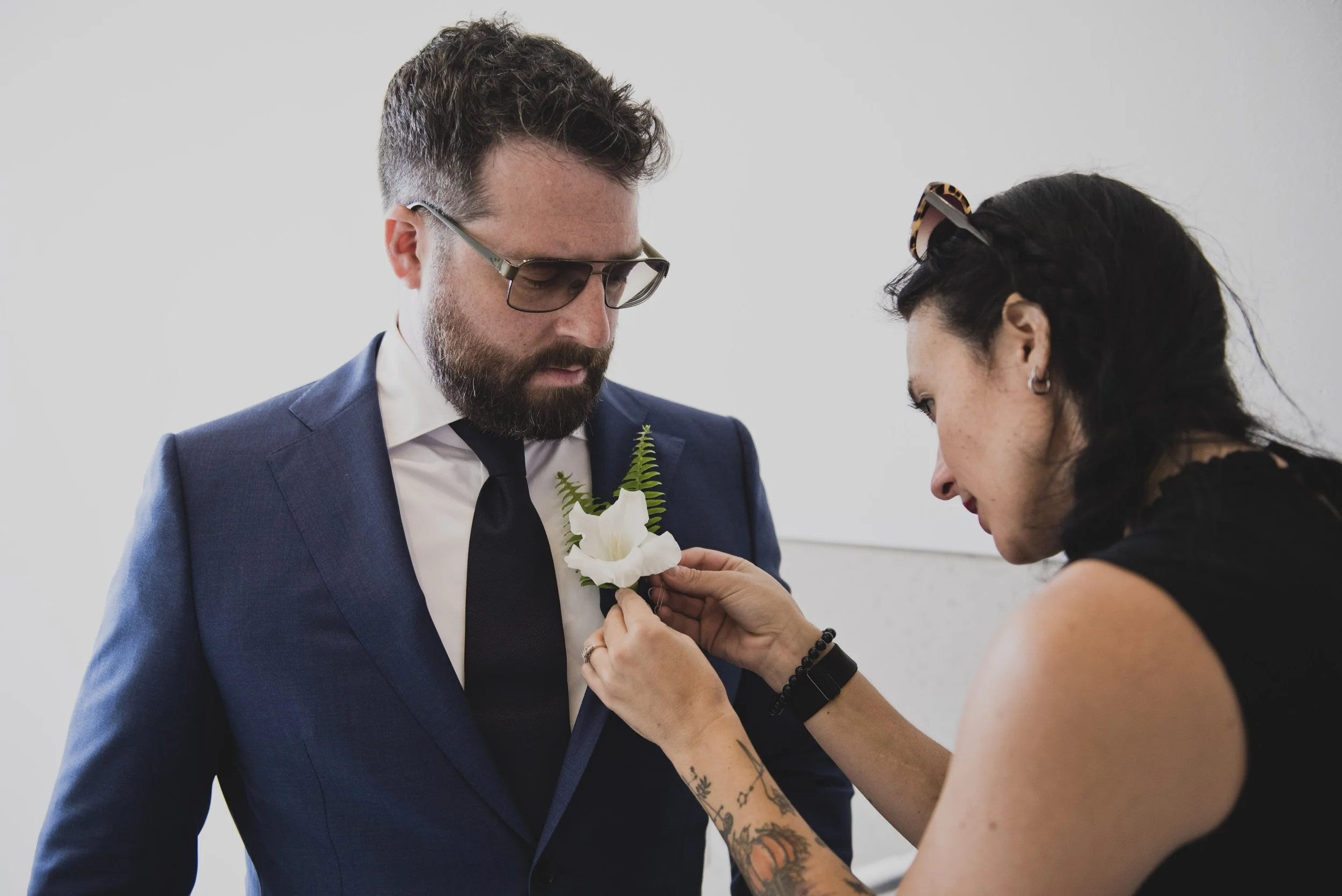 Wedding attendant pinning a white floral boutonniere onto the groom's blue suit before the ceremony.