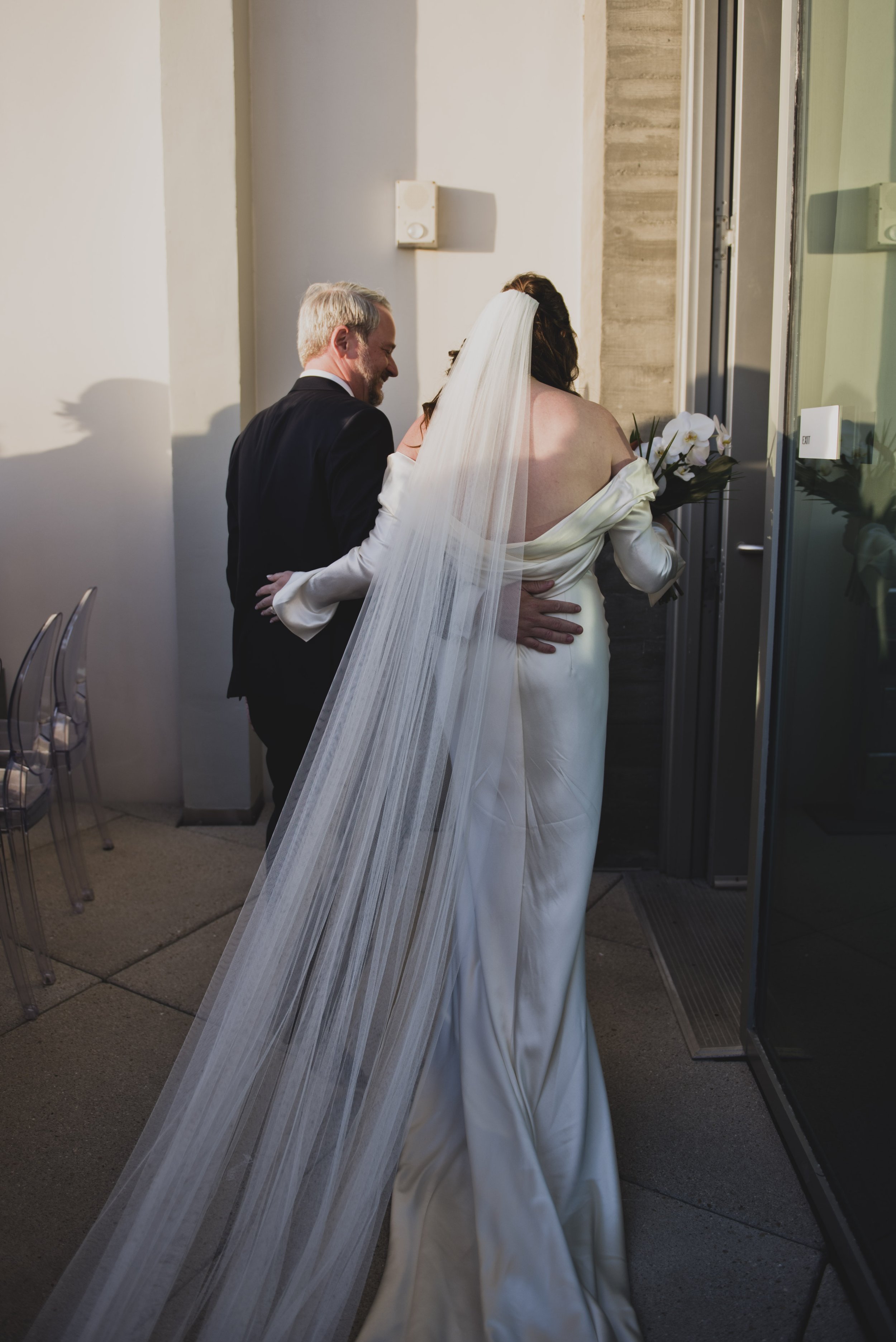 Bride and groom walking arm in arm toward their wedding reception after the ceremony, with the bride's long veil flowing behind her.