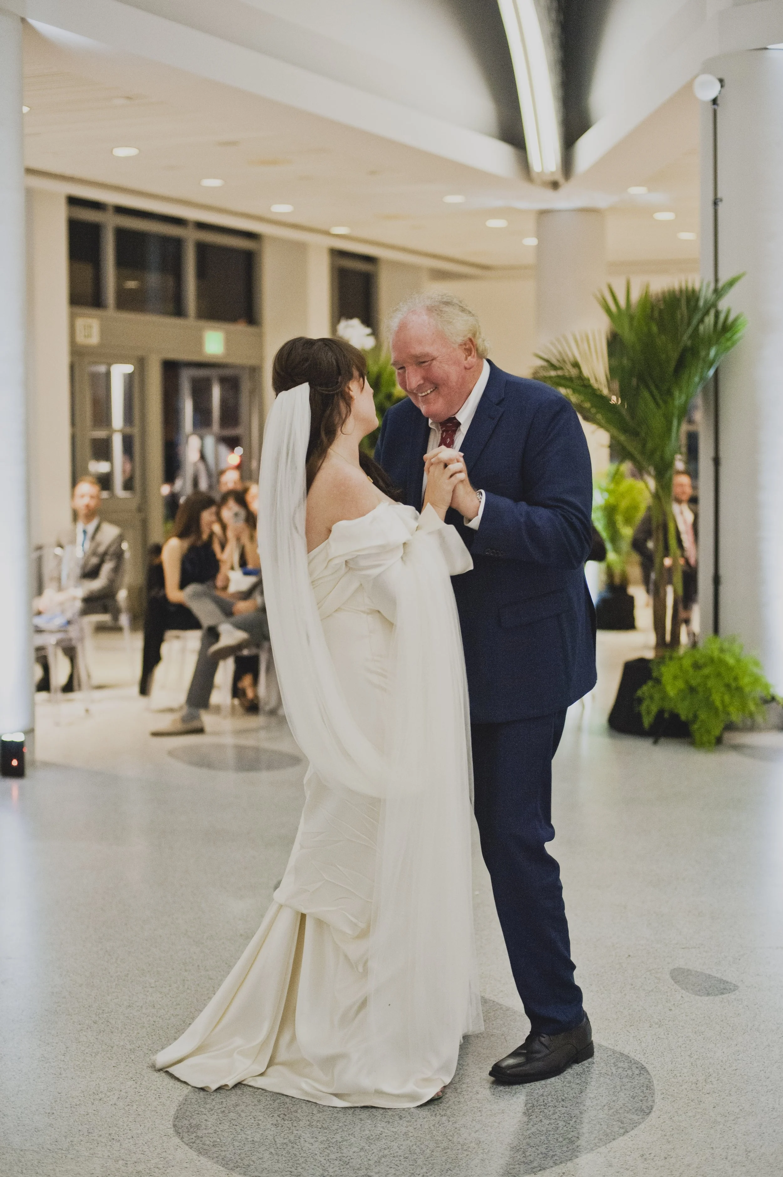 Bride sharing an emotional father-daughter dance with her father during a modern museum wedding reception surrounded by family and guests.