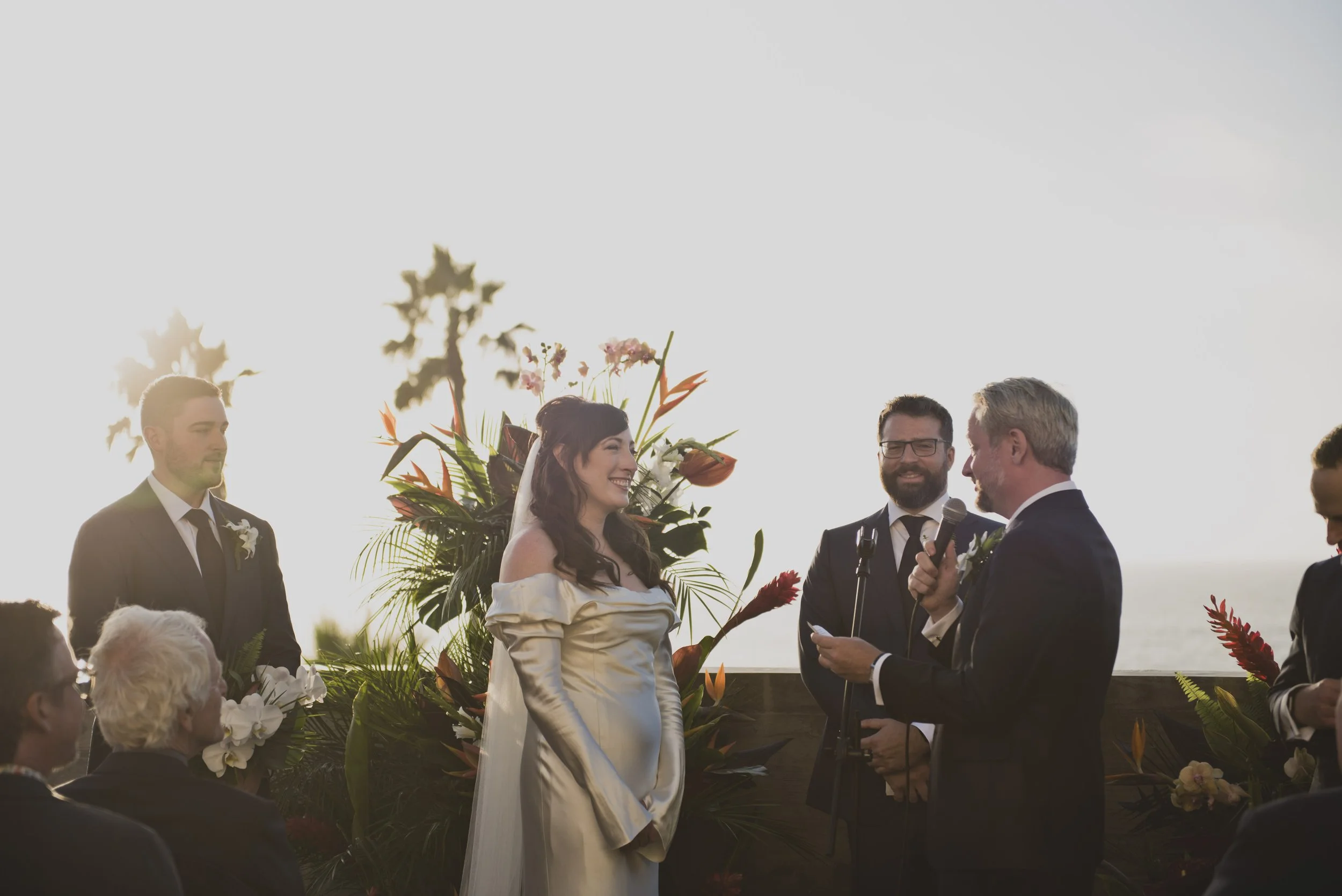 Groom reading his wedding vows to the bride during a modern oceanfront wedding ceremony with tropical floral arrangements framing the altar.