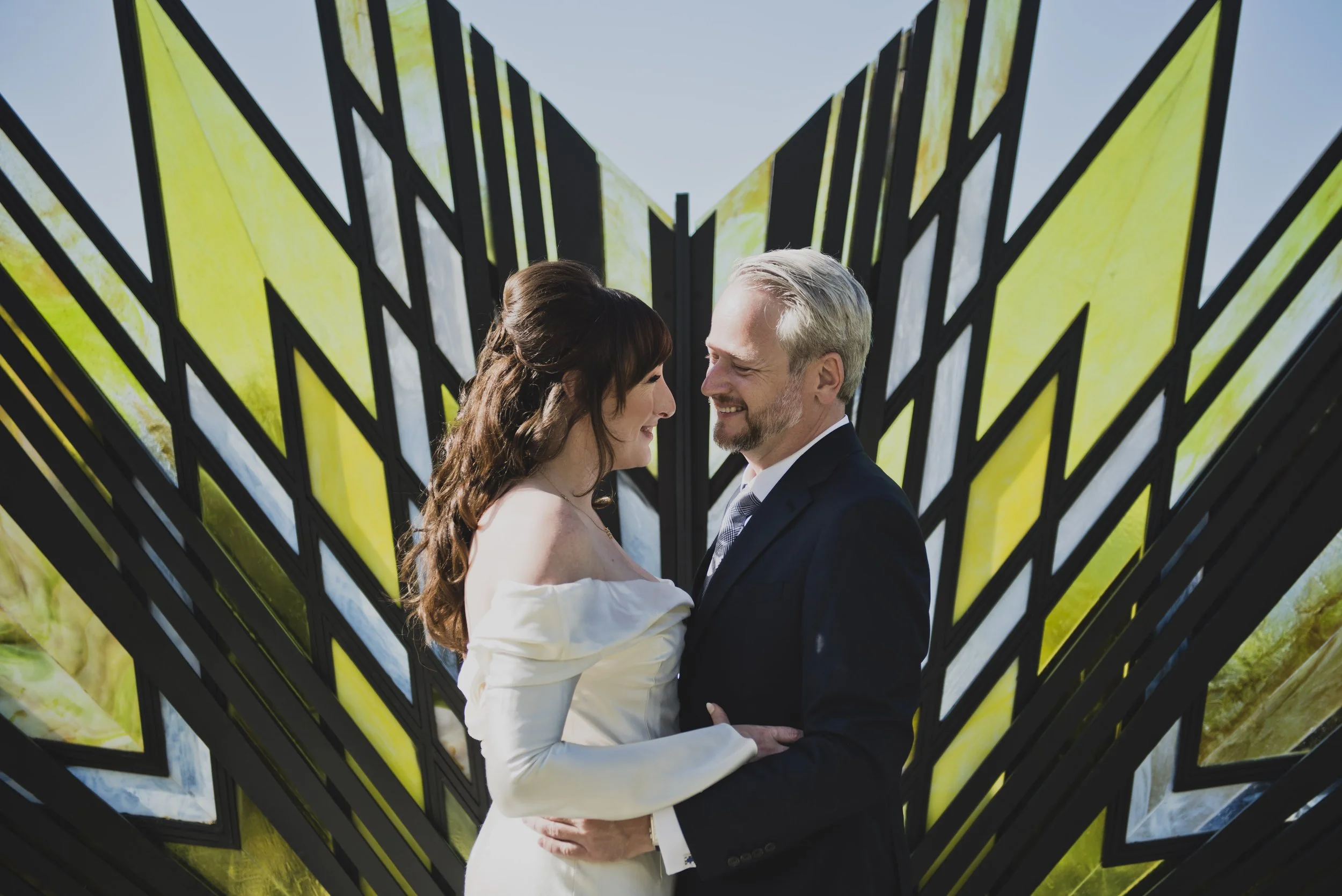 Bride and groom embracing in front of a modern architectural backdrop during their destination wedding portraits.